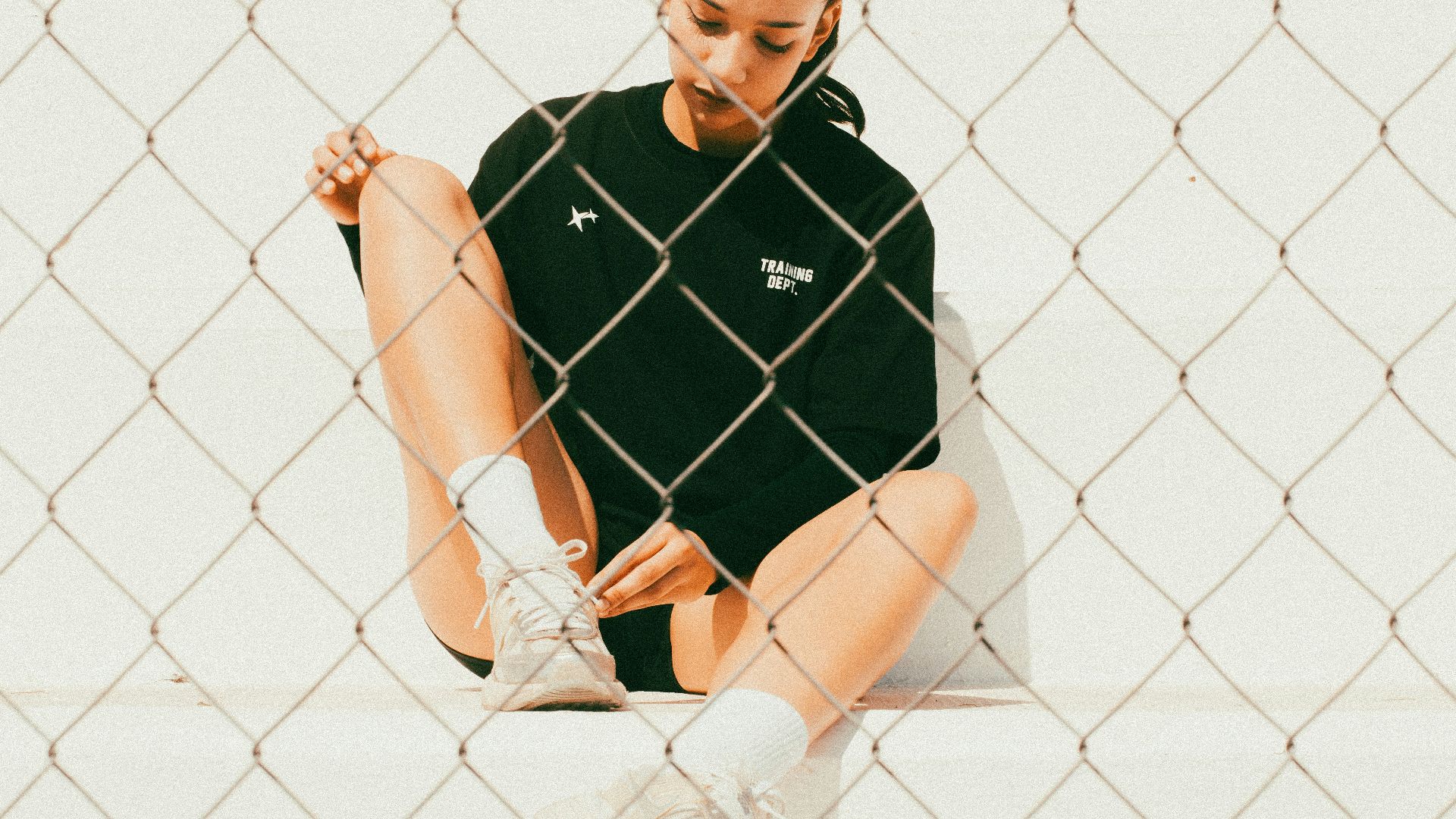 Woman tying shoelace behind wire fence