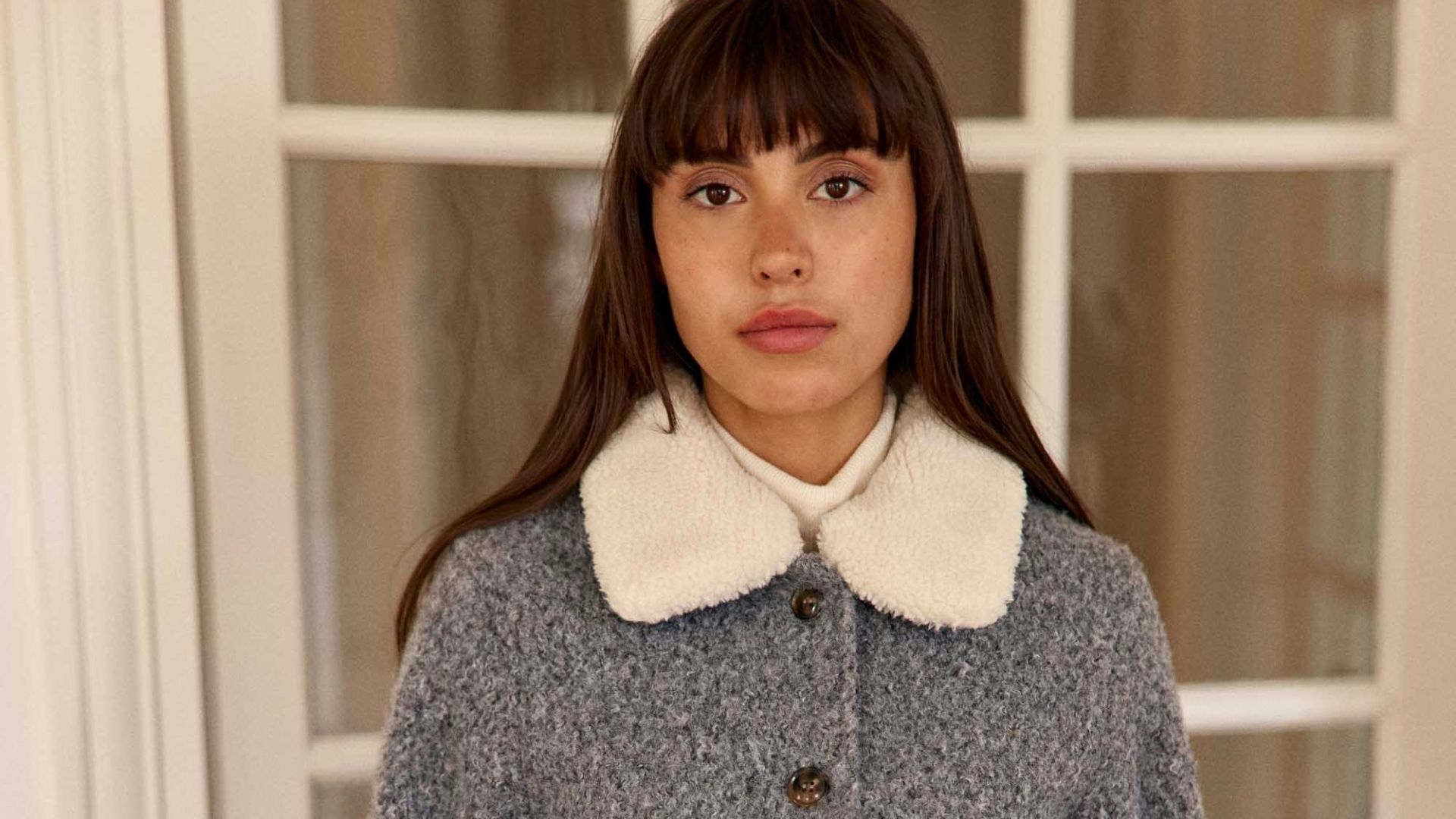 A woman in a grey textured jacket and purple pants.