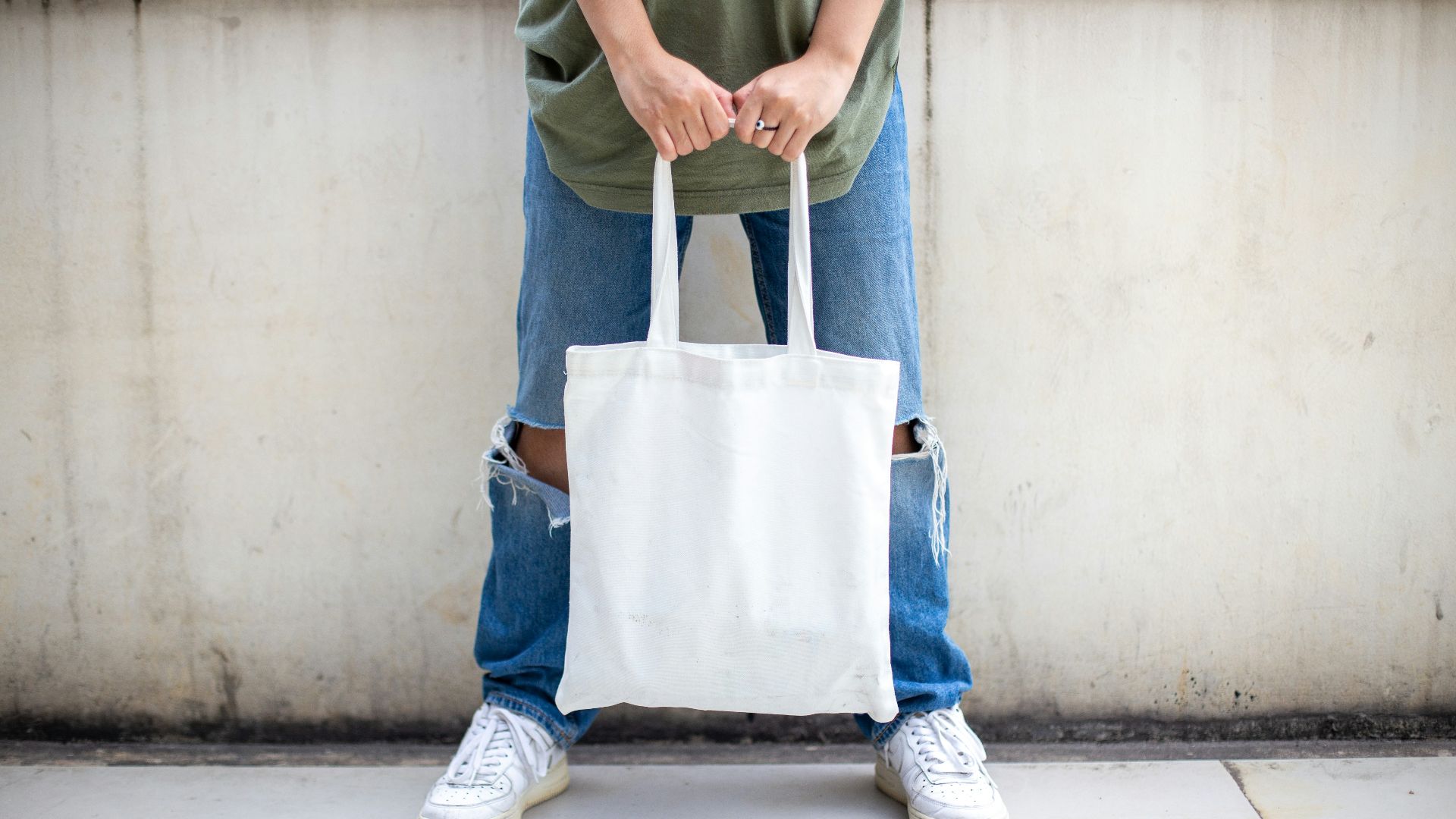 person in blue denim jeans holding white tote bag