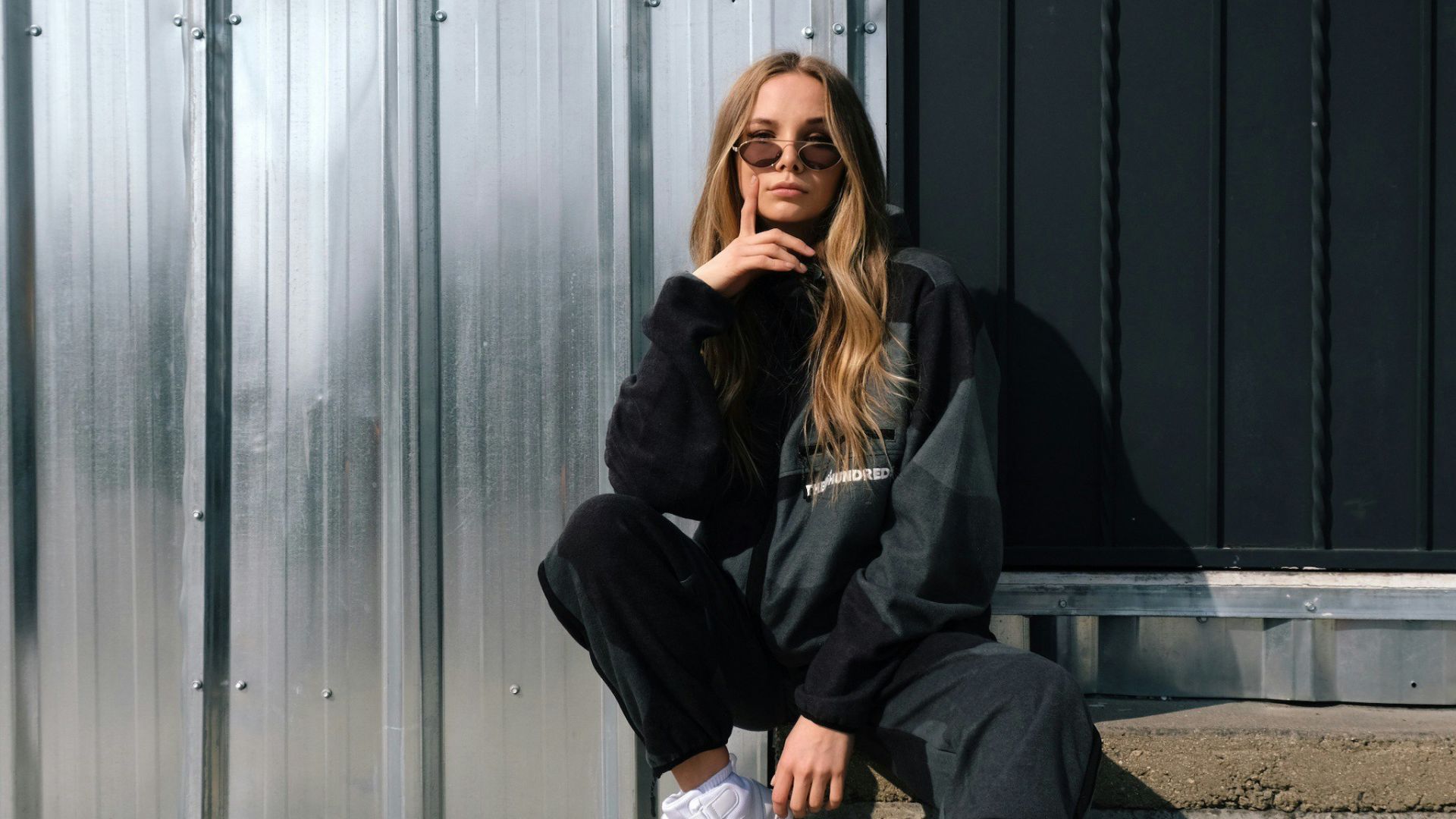 woman in black jacket and white pants sitting on gray concrete floor