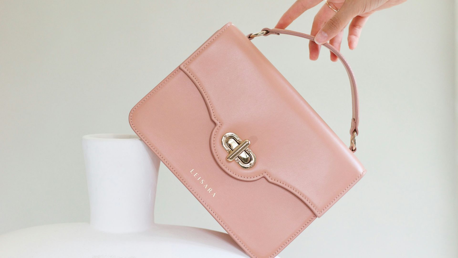 a woman holding a pink purse over a white vase