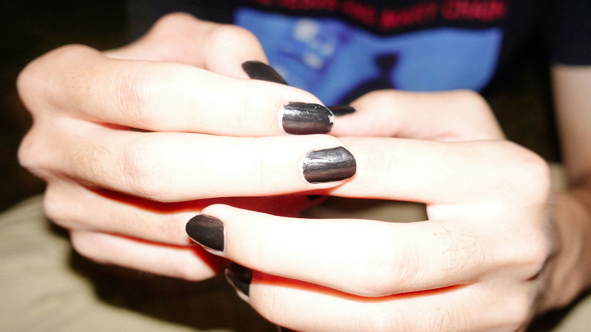 Hands are clasped, showcasing black nail polish.