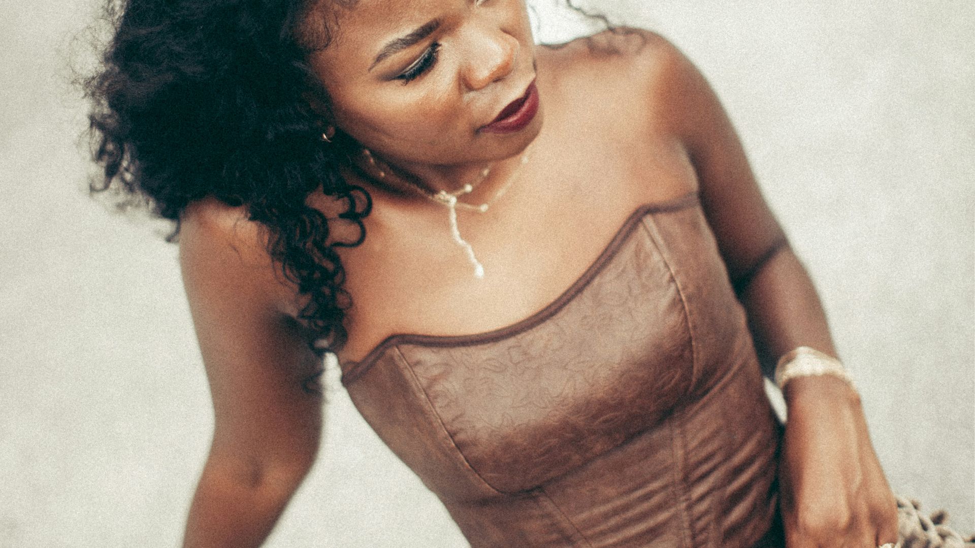 A woman poses in brown corset and pants.
