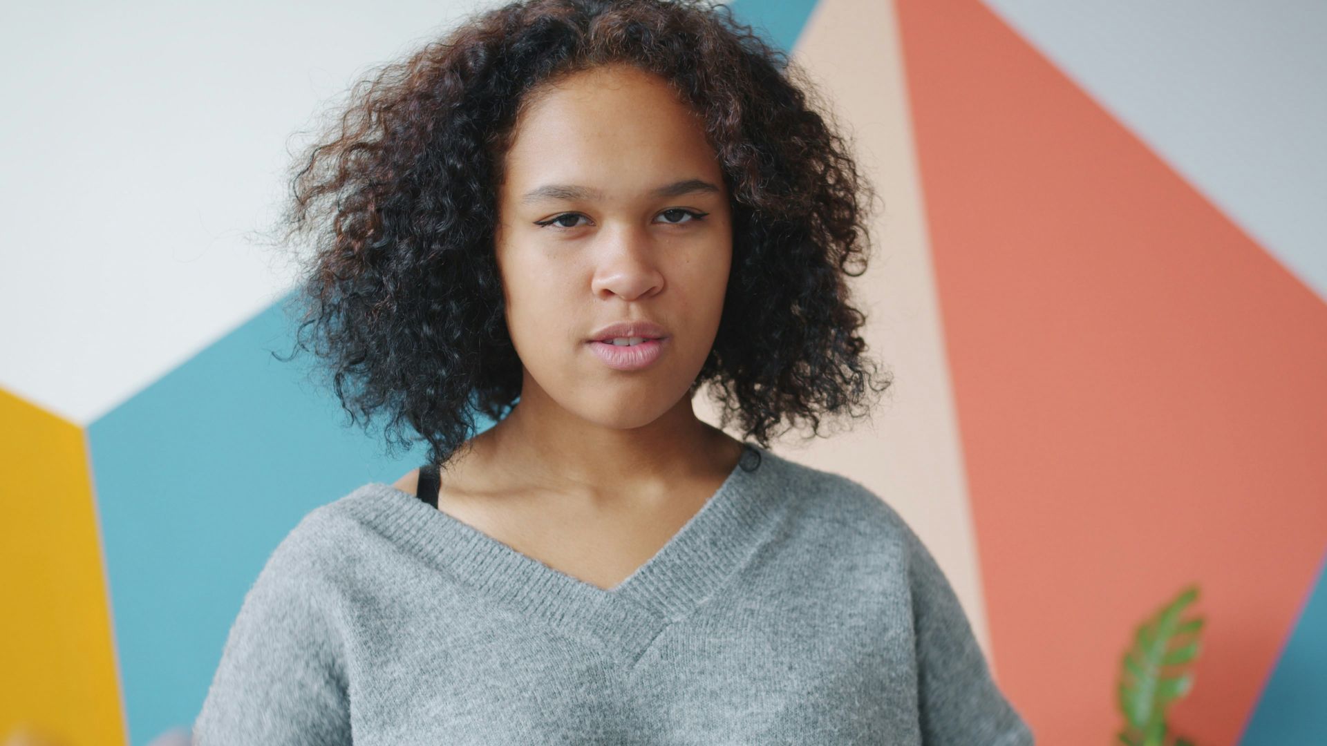 Young woman with curly hair against colorful wall.