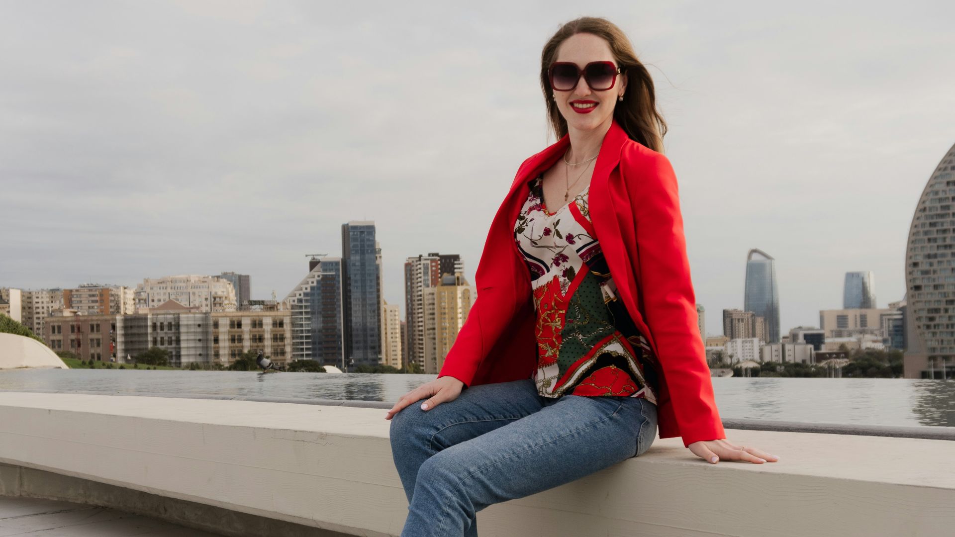 Woman in red jacket sitting on ledge overlooking cityscape