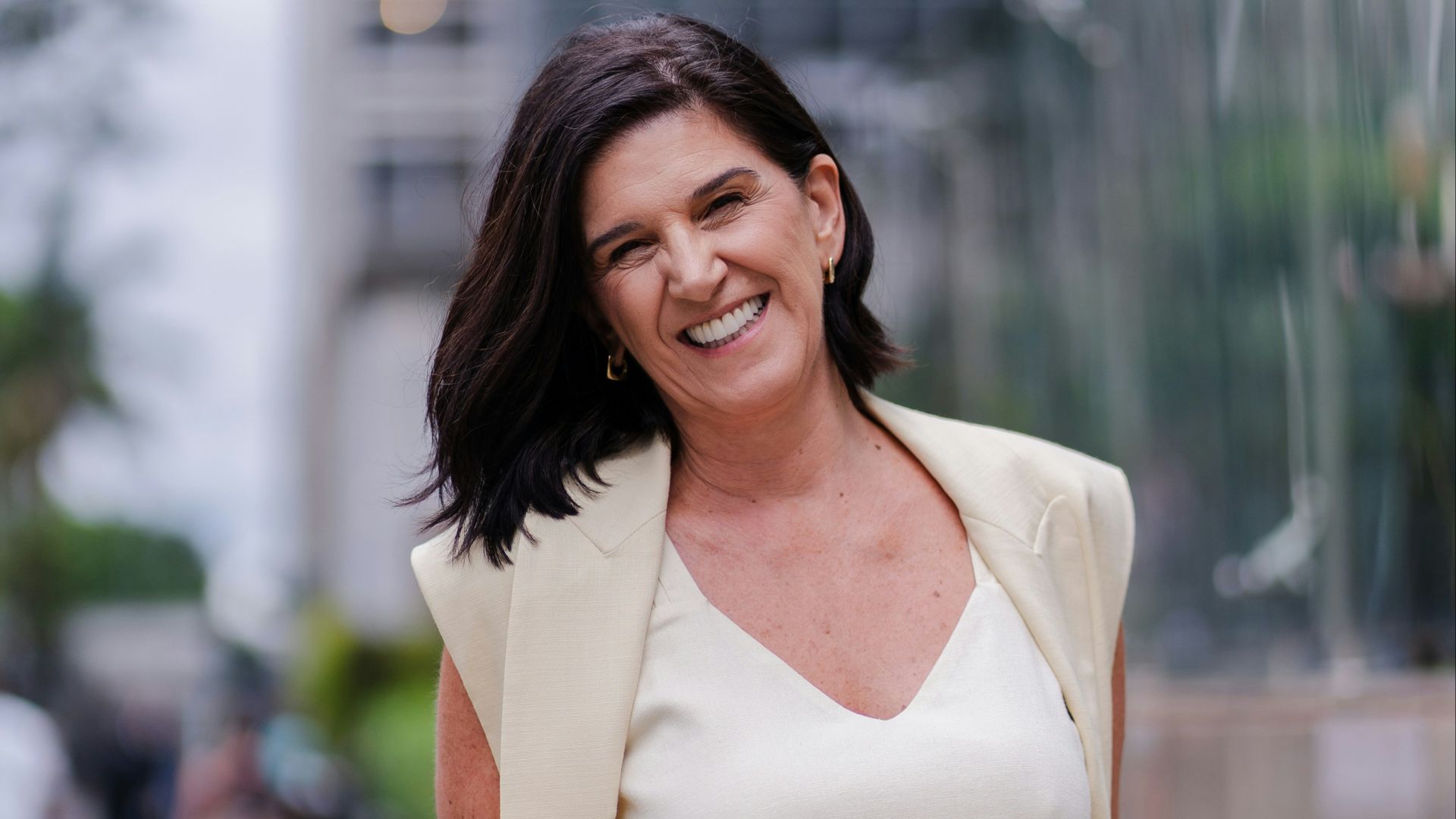 A smiling woman in a cream suit stands outdoors.