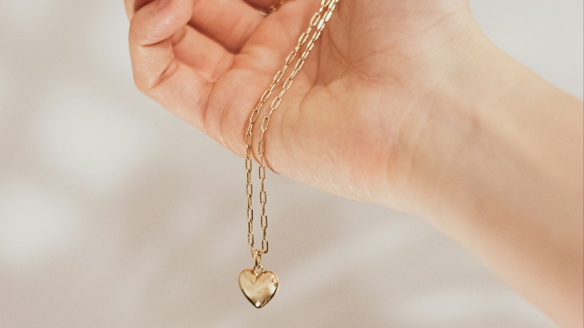 a hand holding a gold heart charm on a chain