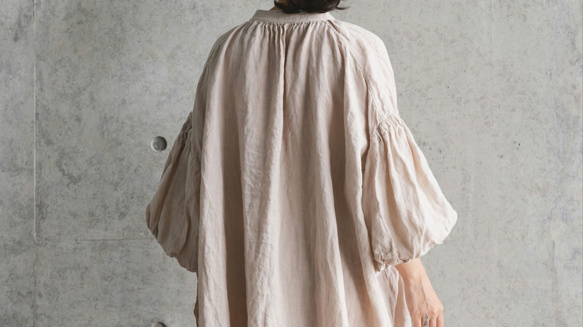 Woman in straw hat and linen dress stands against wall