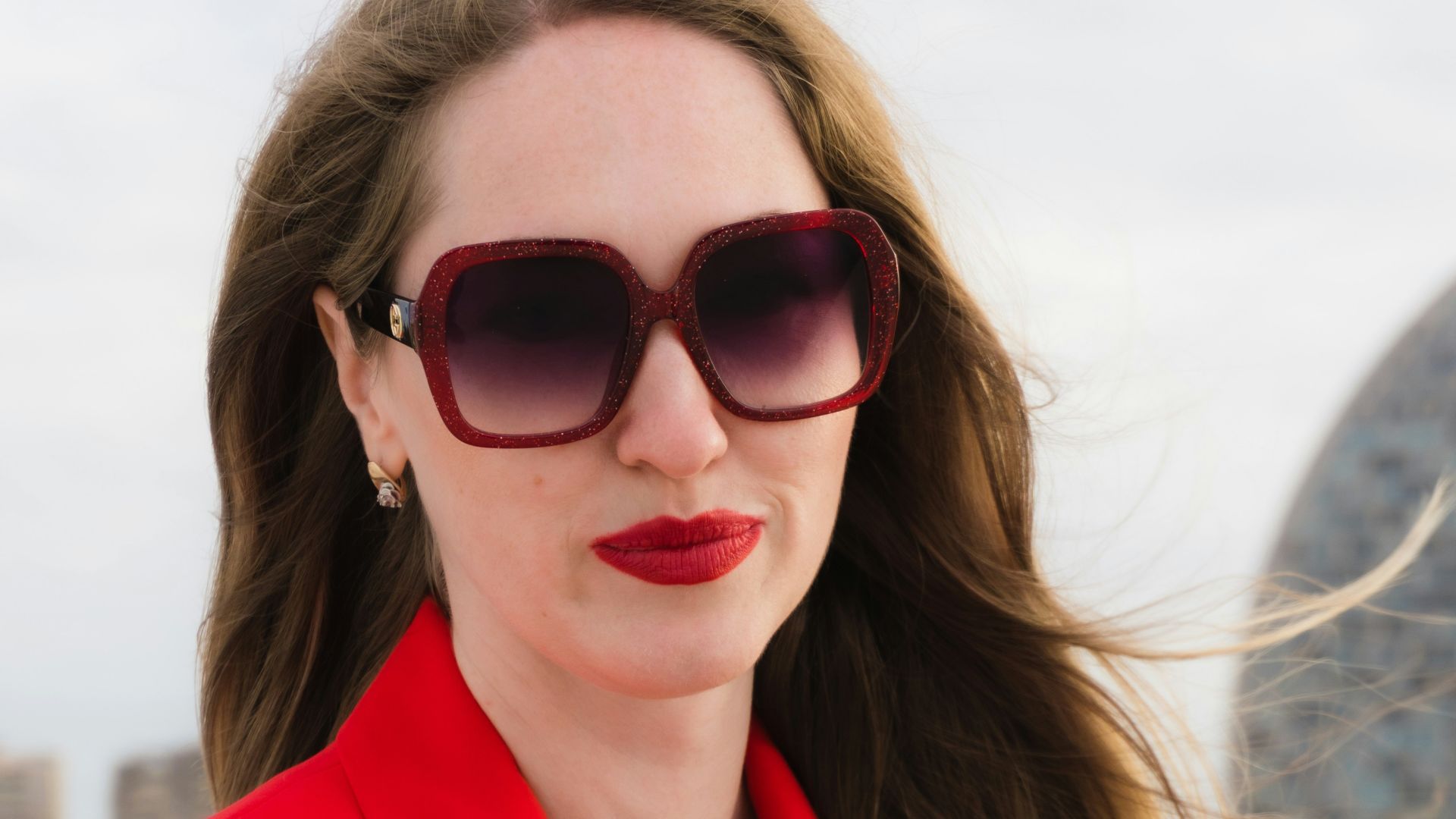 Woman in red blazer and large sunglasses outdoors