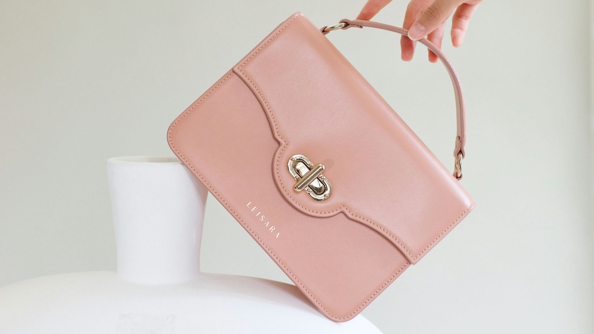 a woman holding a pink purse over a white vase