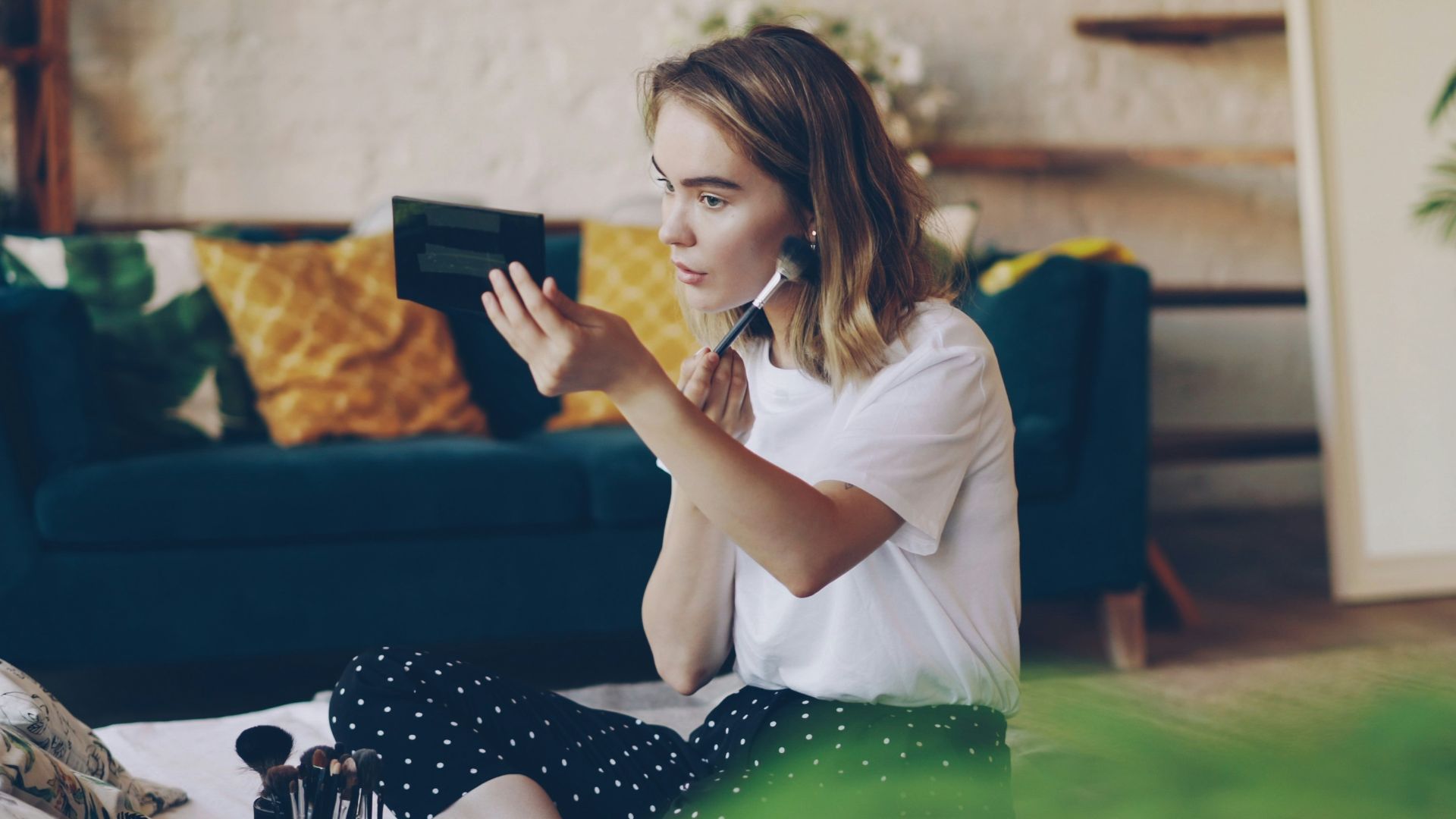 A young woman applying makeup in a bright room.