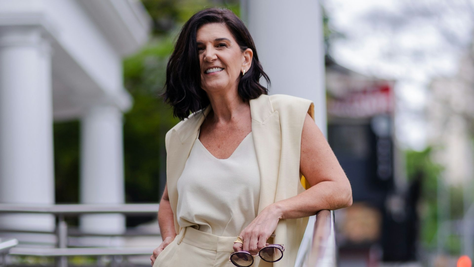 Woman in beige suit leaning on railing outside building