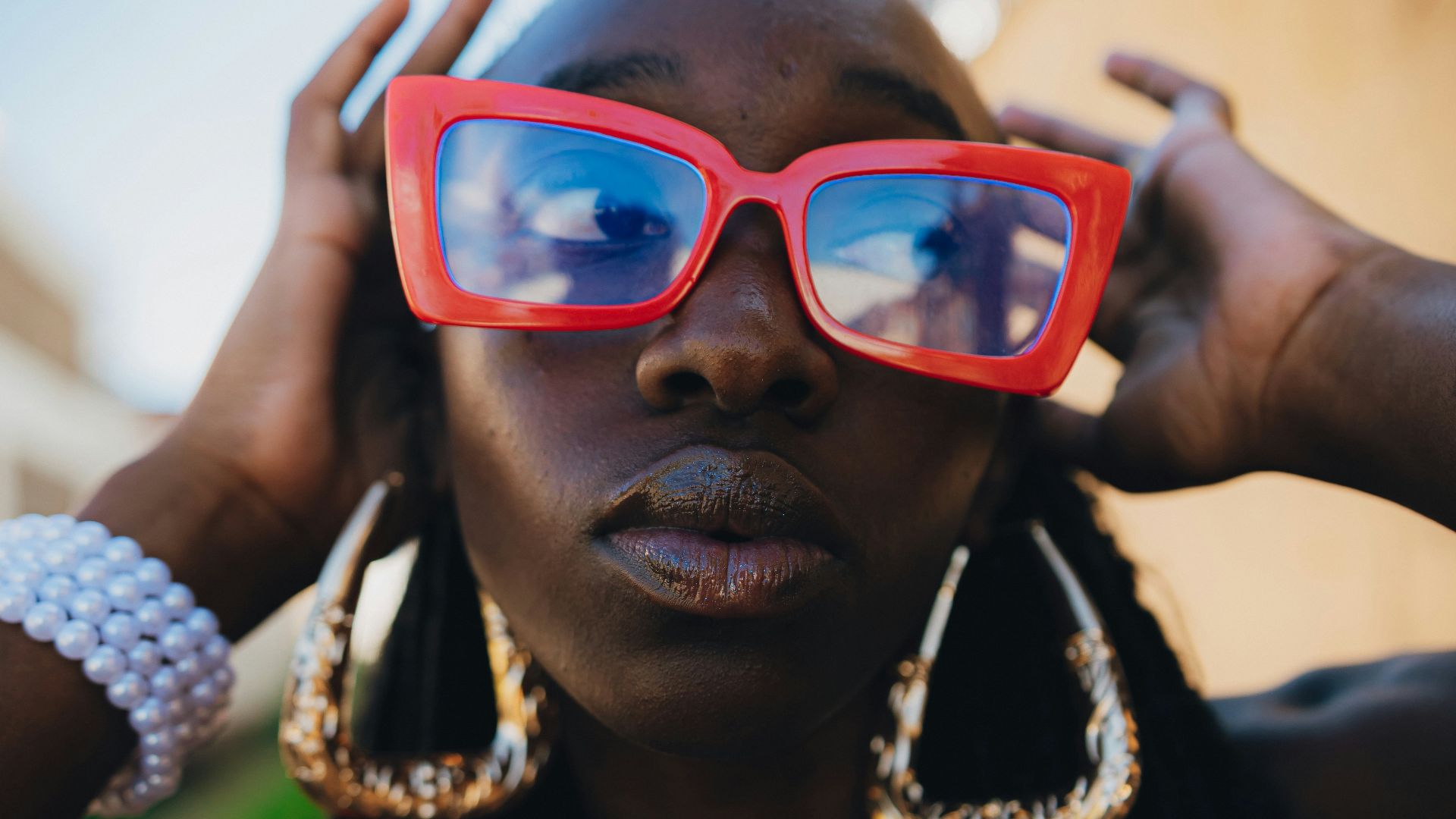 Woman wearing large red sunglasses and gold earrings