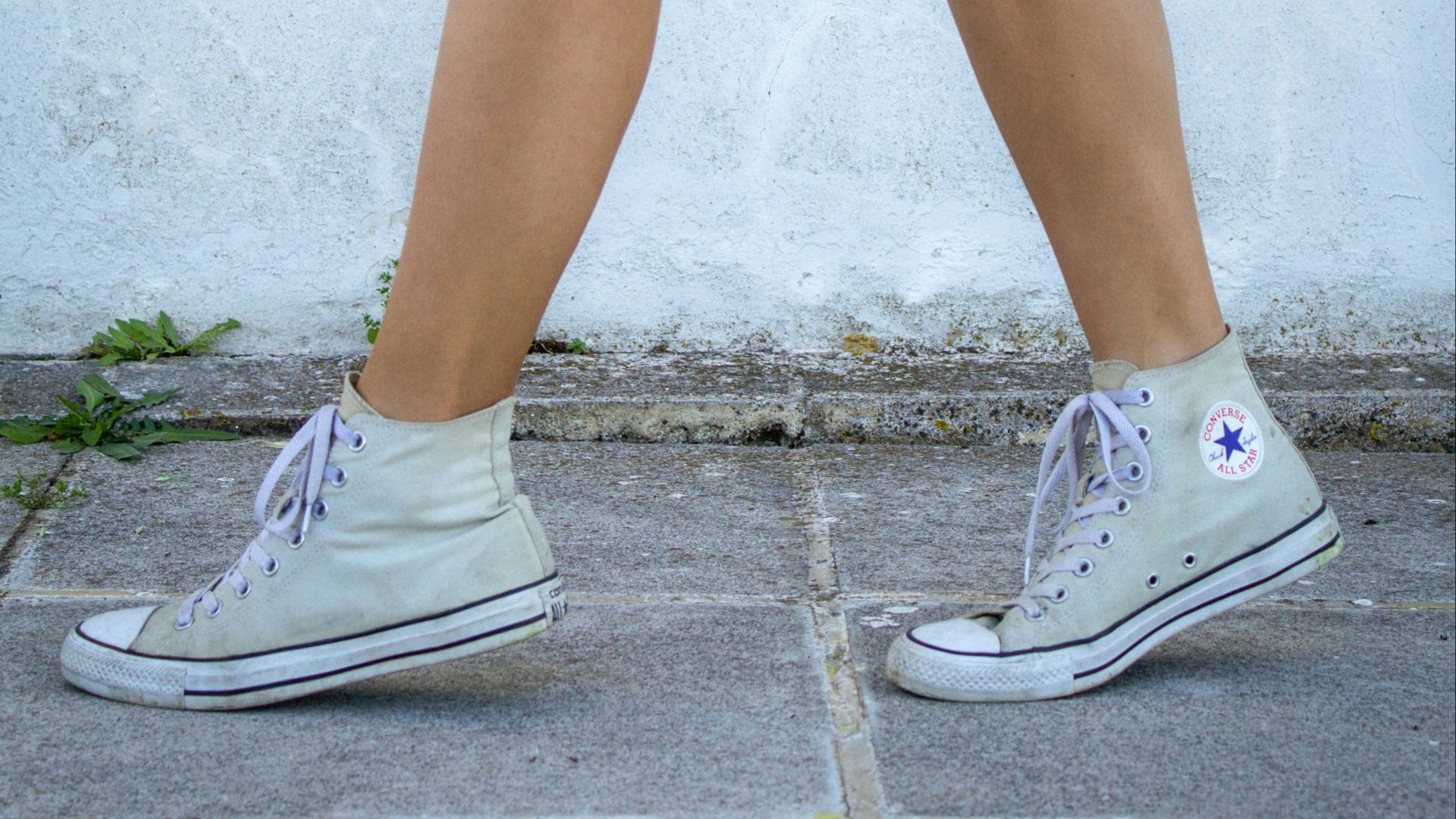 a woman walking down a sidewalk wearing tennis shoes