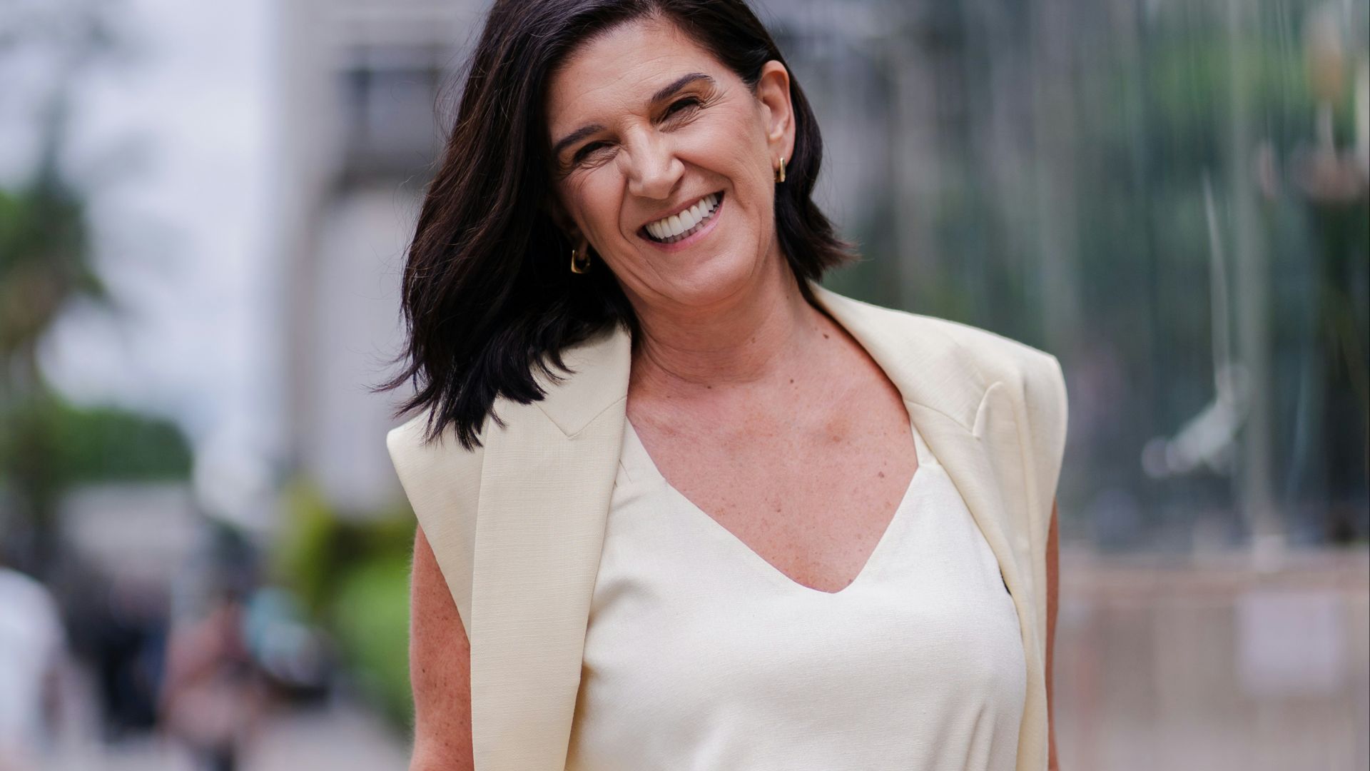 A smiling woman in a cream suit stands outdoors.