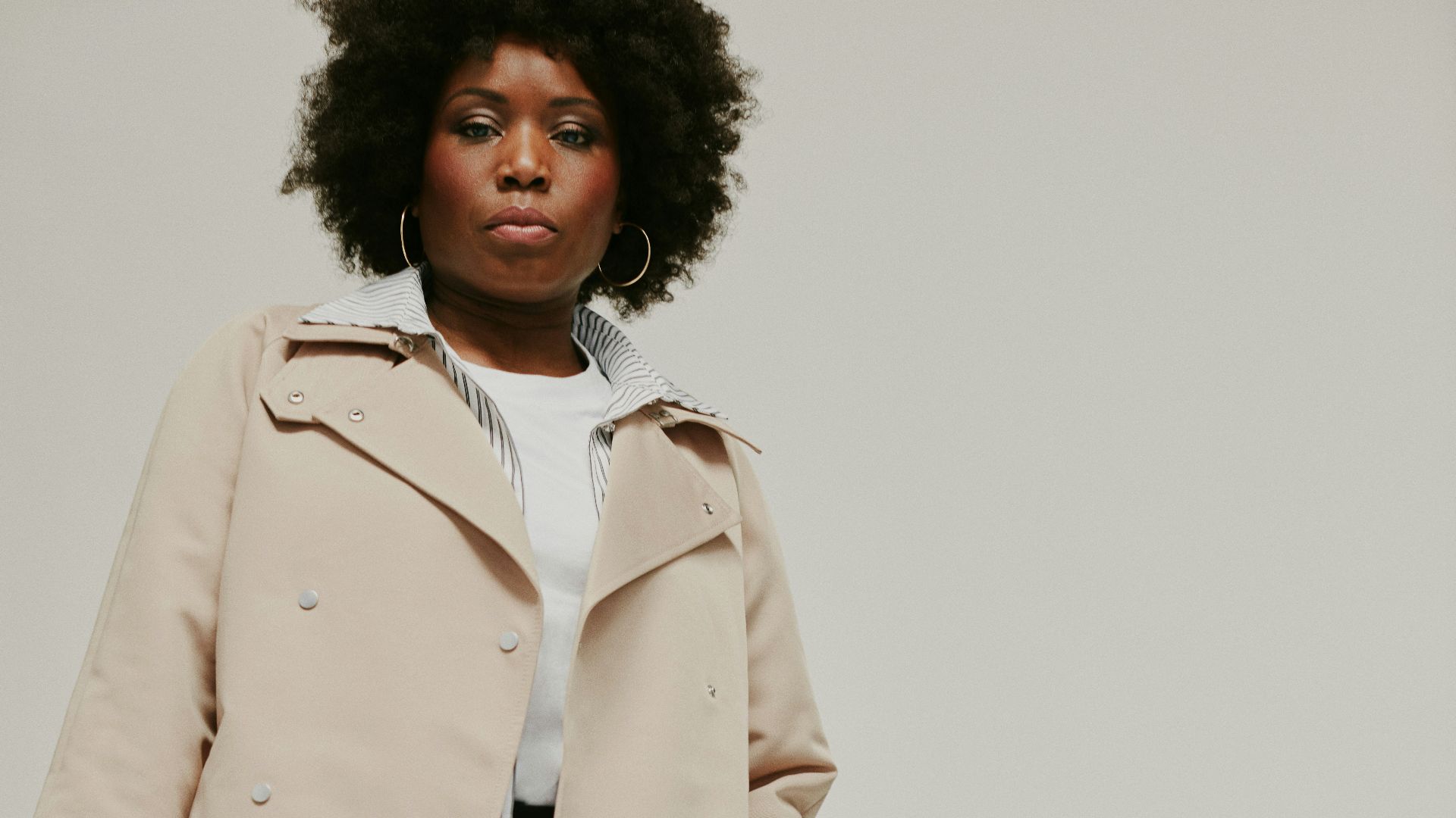 a woman in a trench coat holding a pink purse