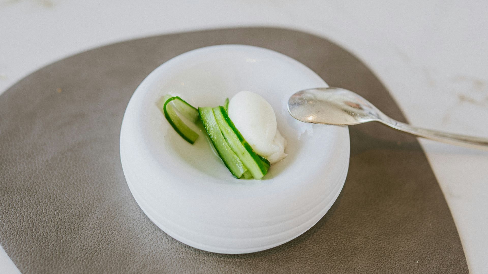 A small dish with cucumber and cream with a spoon.
