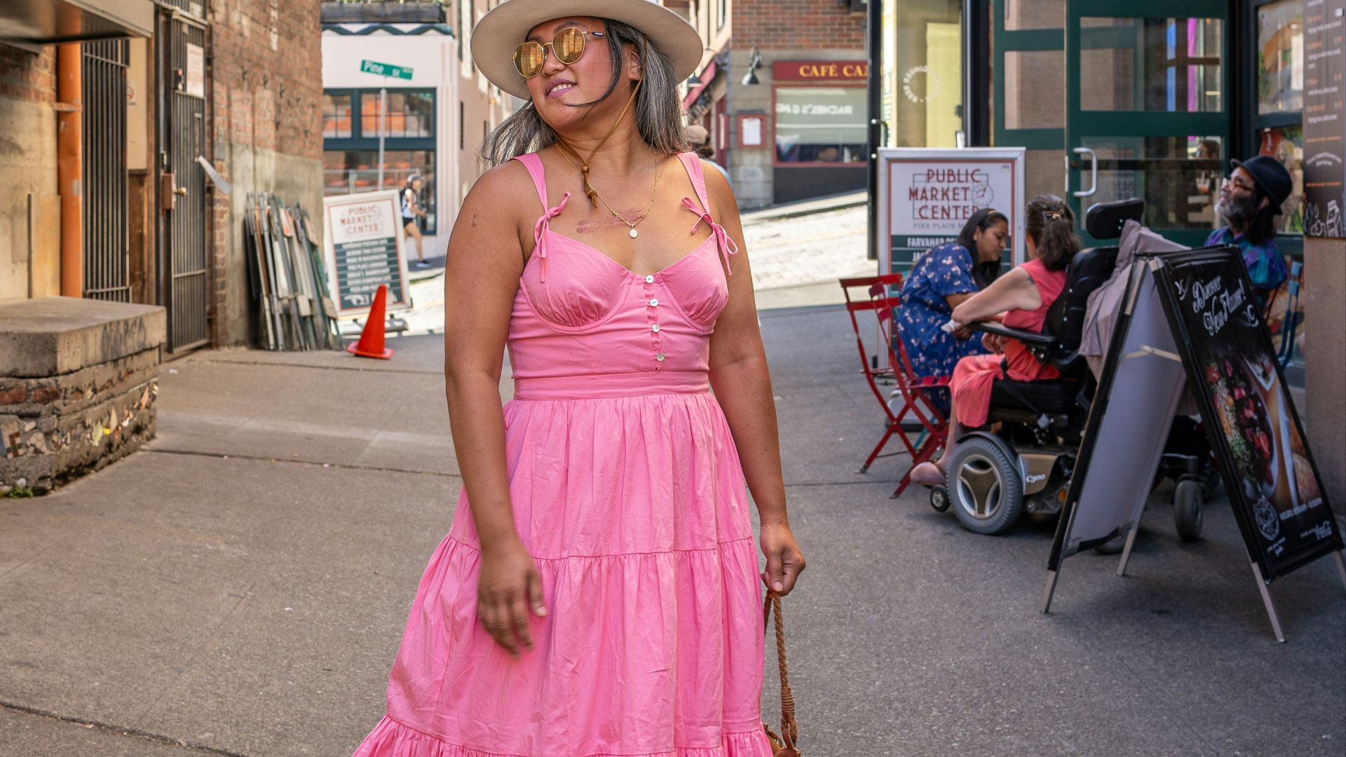 a woman in a pink dress and hat walking down a street