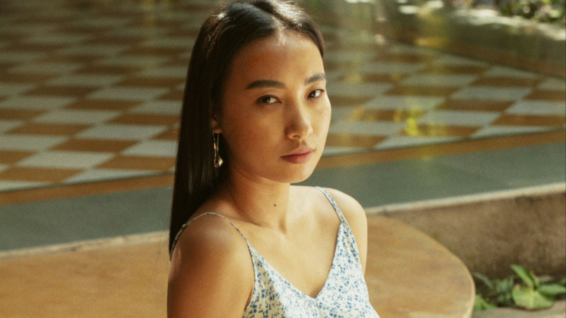 A young woman in a floral jumpsuit sits outdoors.