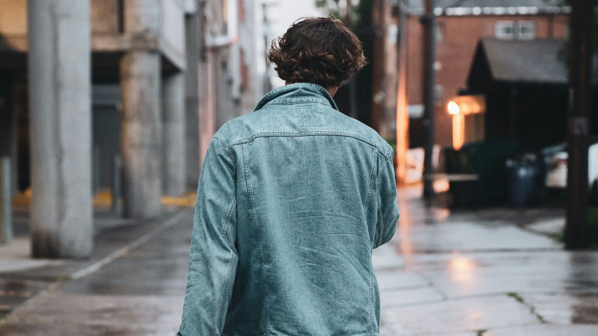 man in green hoodie standing on sidewalk during daytime