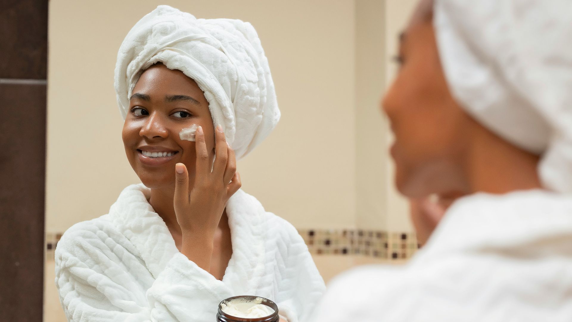 a woman with a towel on her head and a jar of cream on her face