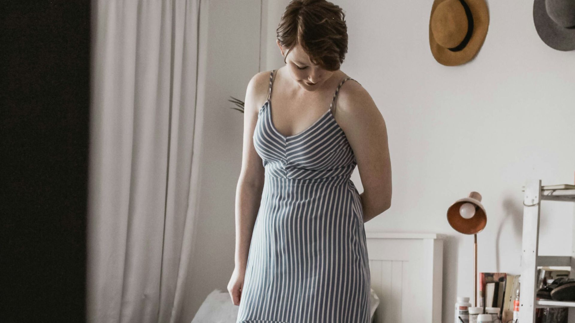 woman wearing black and white striped spaghetti strap dress standing beside bed frame