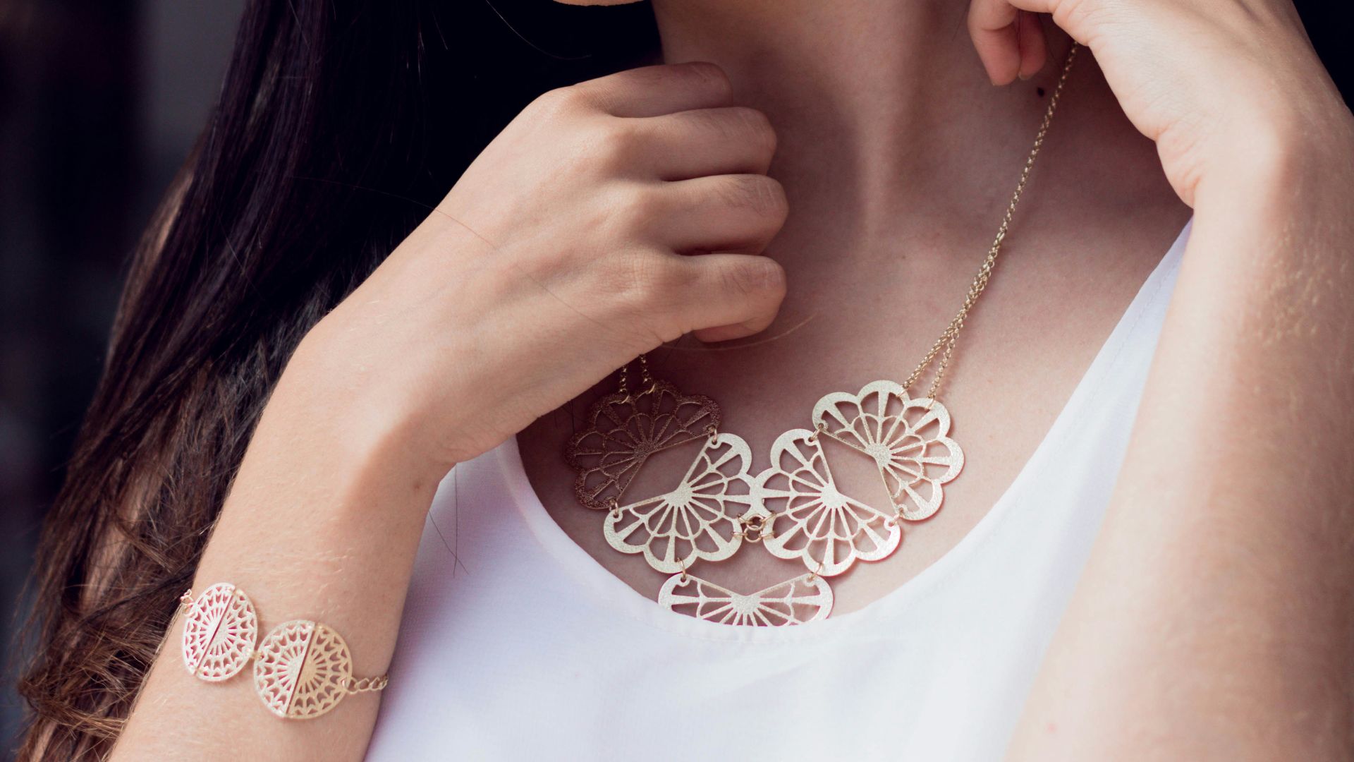 A woman in a white top is wearing a necklace and earrings