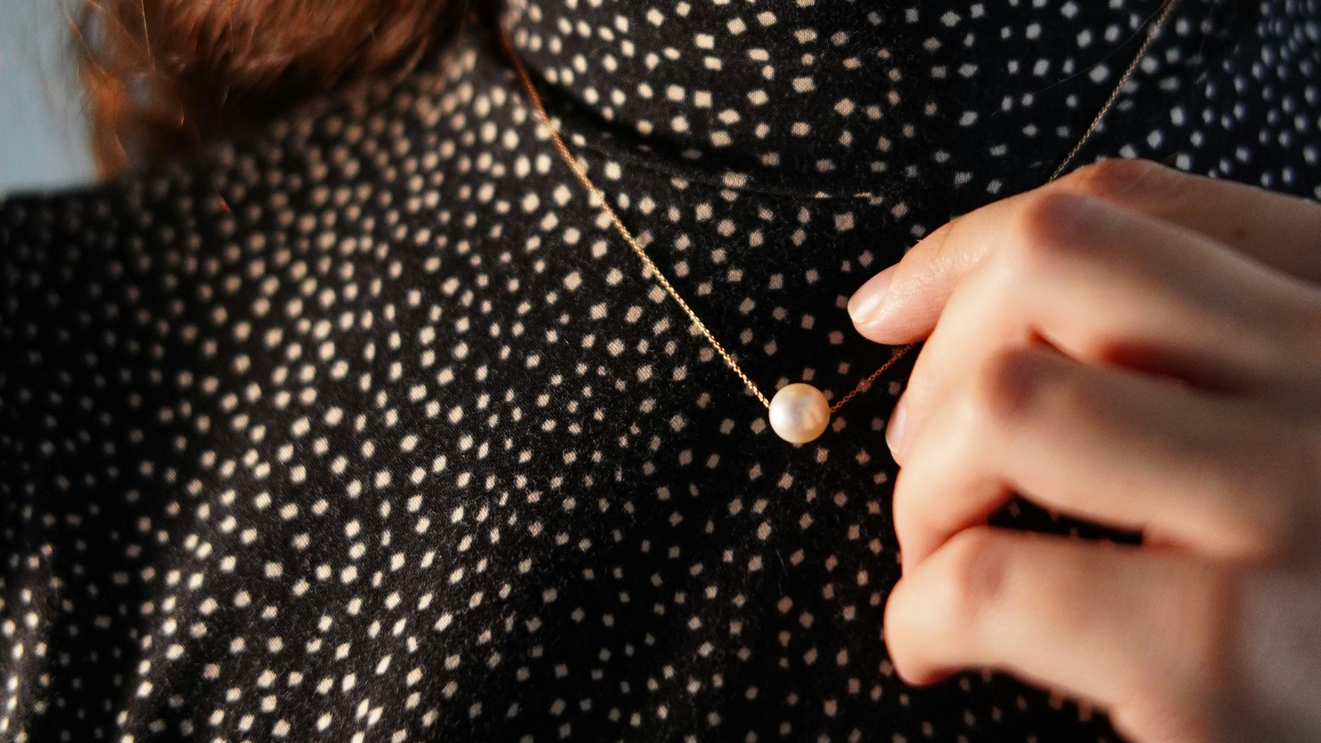 Woman in polka dot dress touches pearl necklace