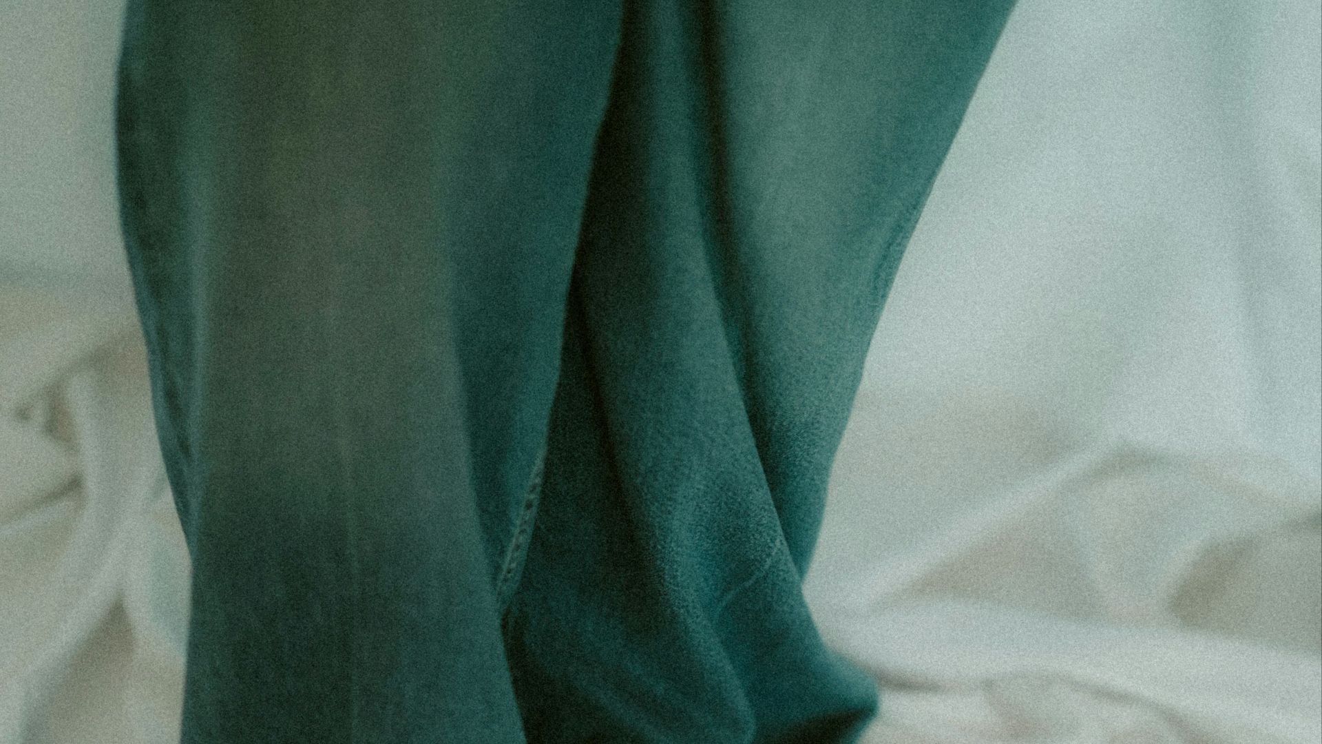 Bare feet in jeans on a wrinkled white sheet.