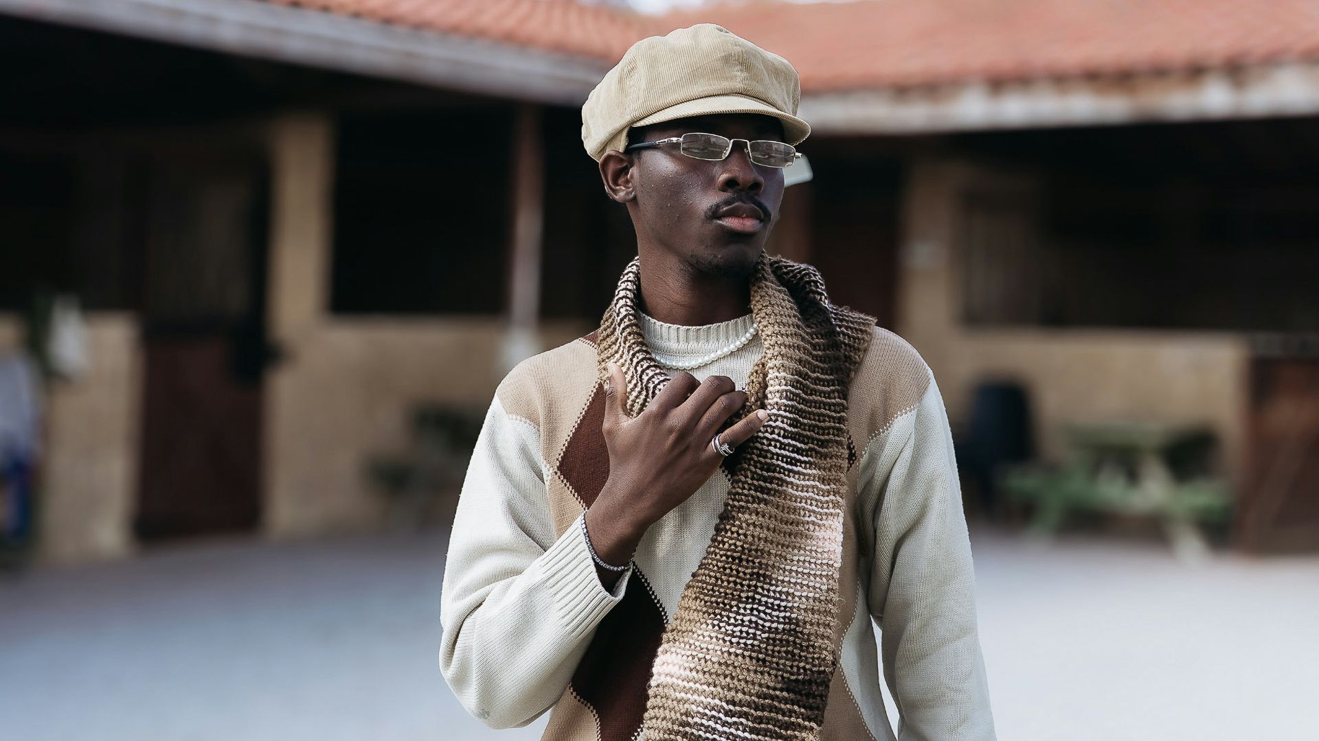 Man in cap and scarf stands outside building