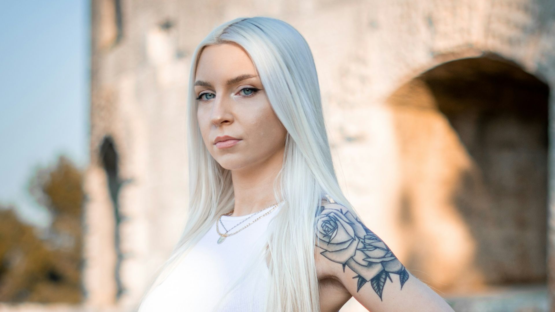 woman in white tank top and blue denim shorts standing near brown wall during daytime