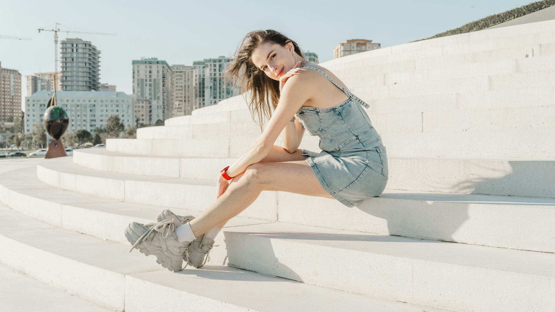 Young woman in denim dress sitting on white steps