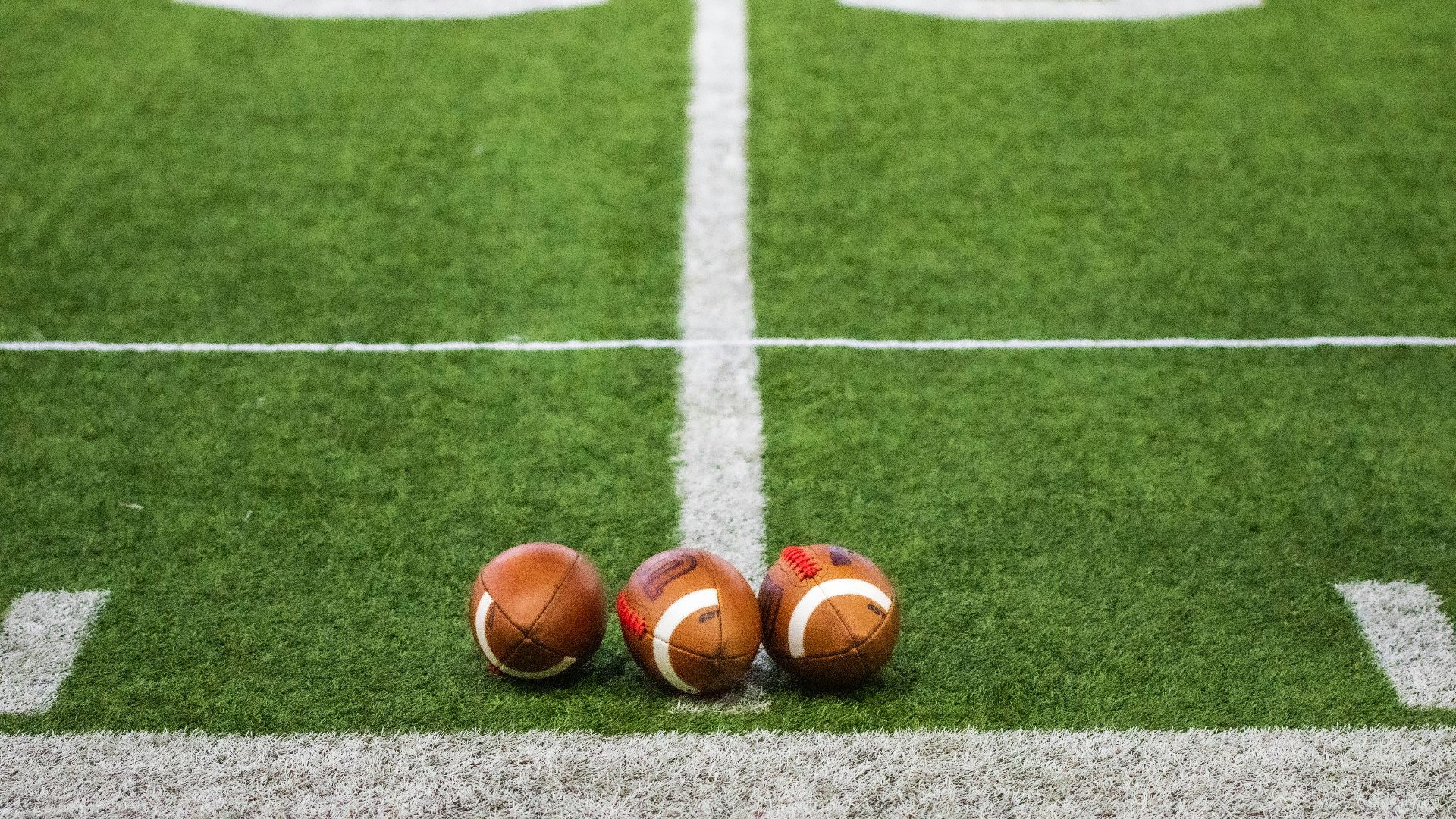 Three footballs sitting on a football field