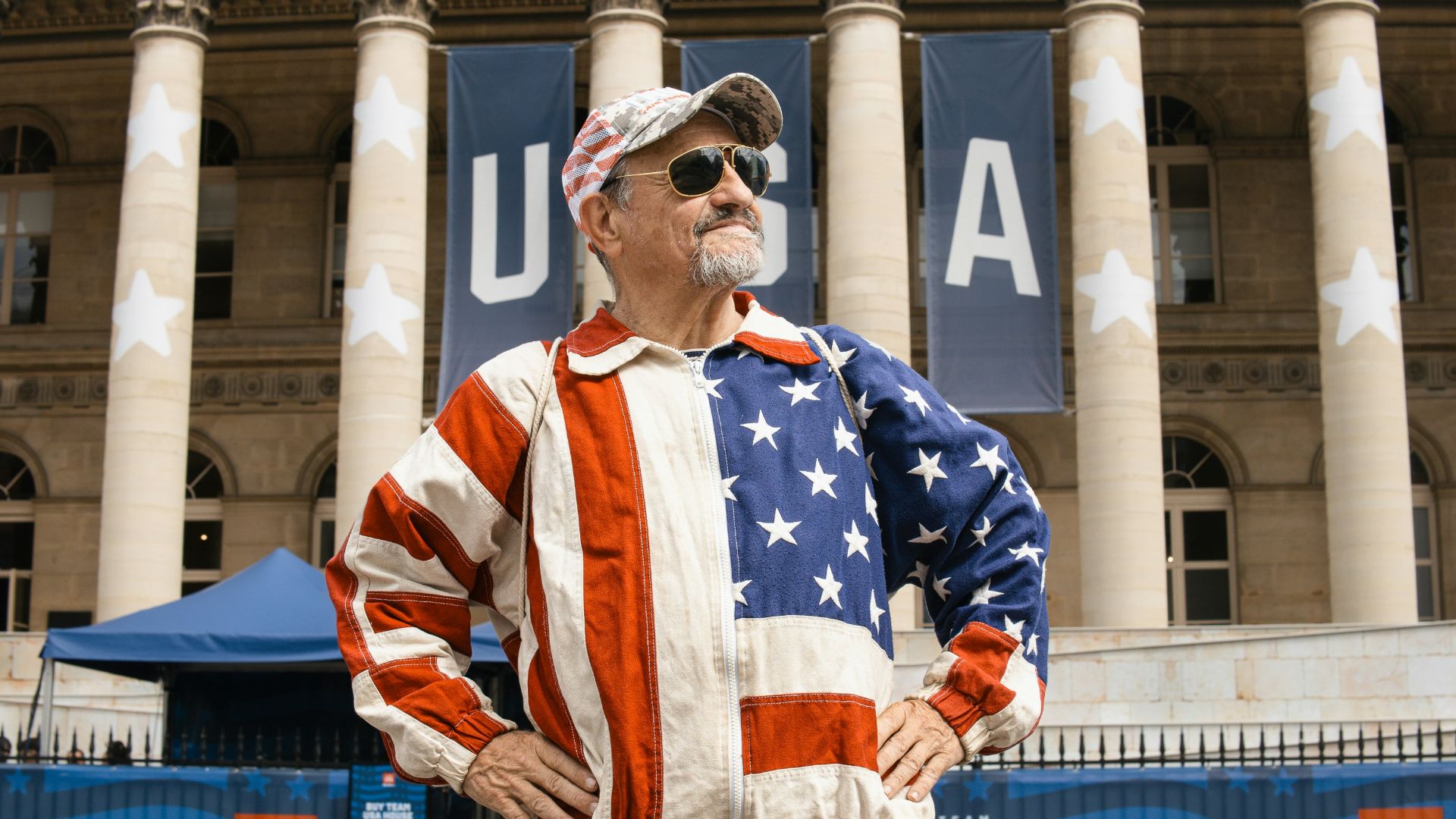 A man in an american flag jacket standing in front of a building