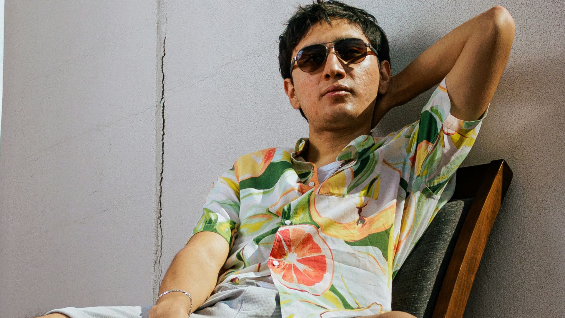 Man in hawaiian shirt and shorts sitting on chair.