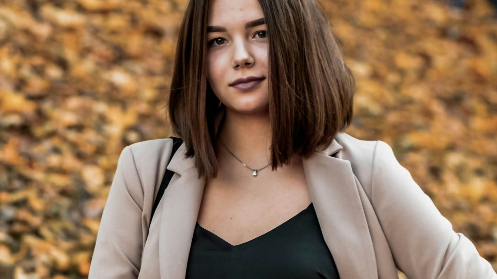 woman in black tank top and beige blazer standing on dried leaves