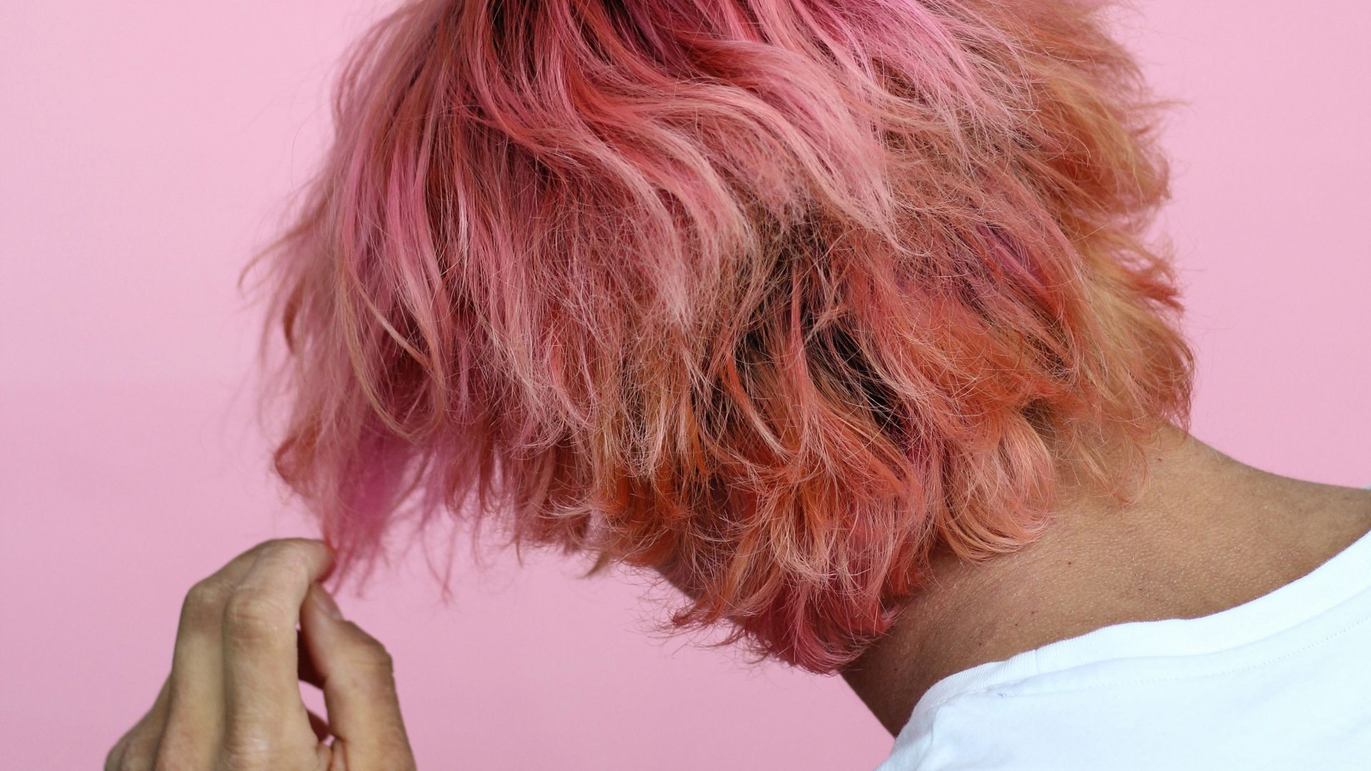 person in white top touch hair with pink dye