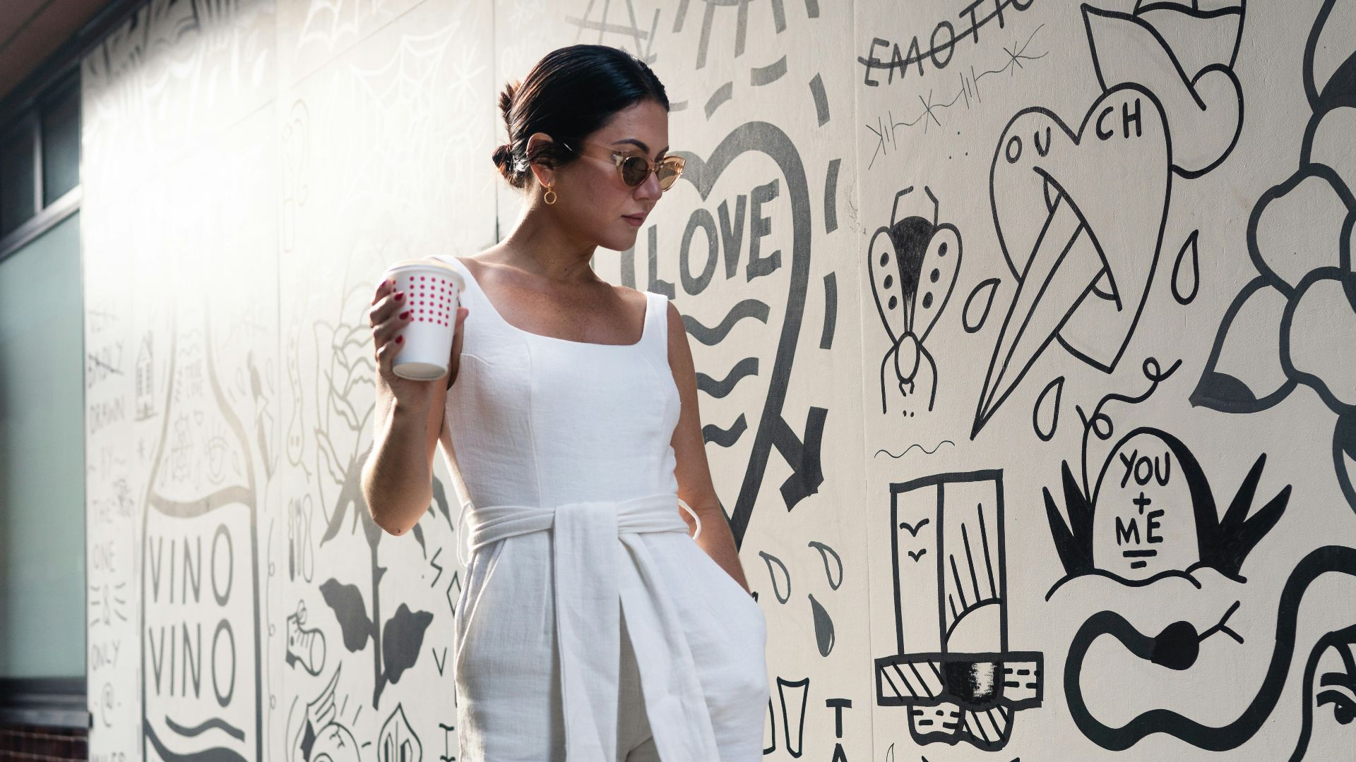 woman holding cup walking beside wall