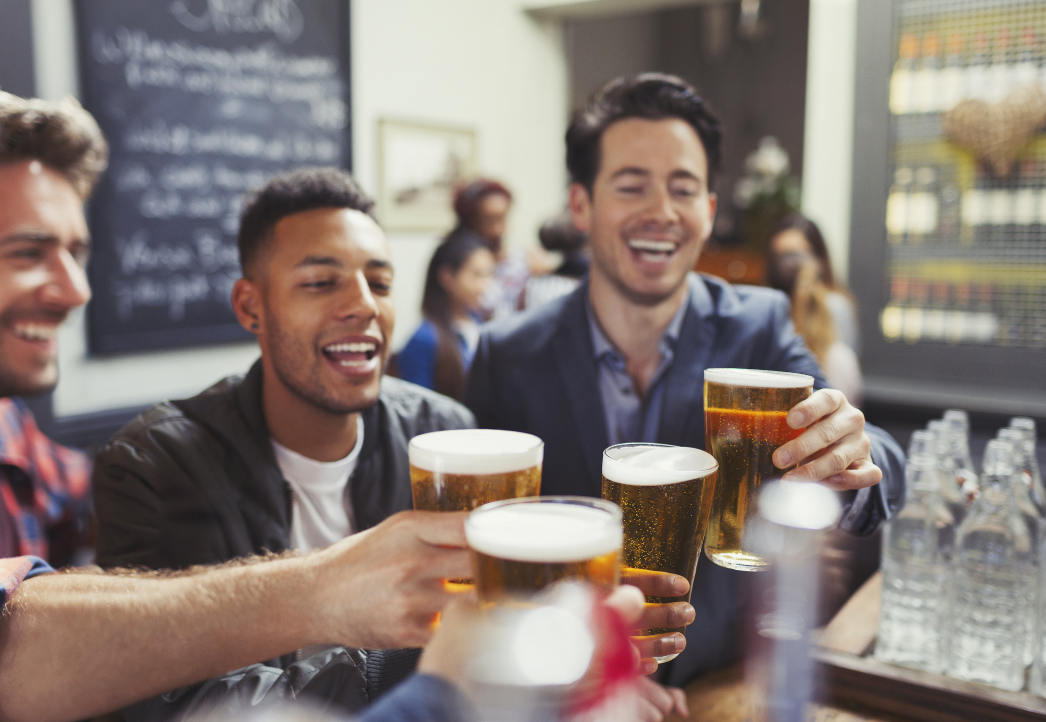 Male friends toasting beer glasses at bar.