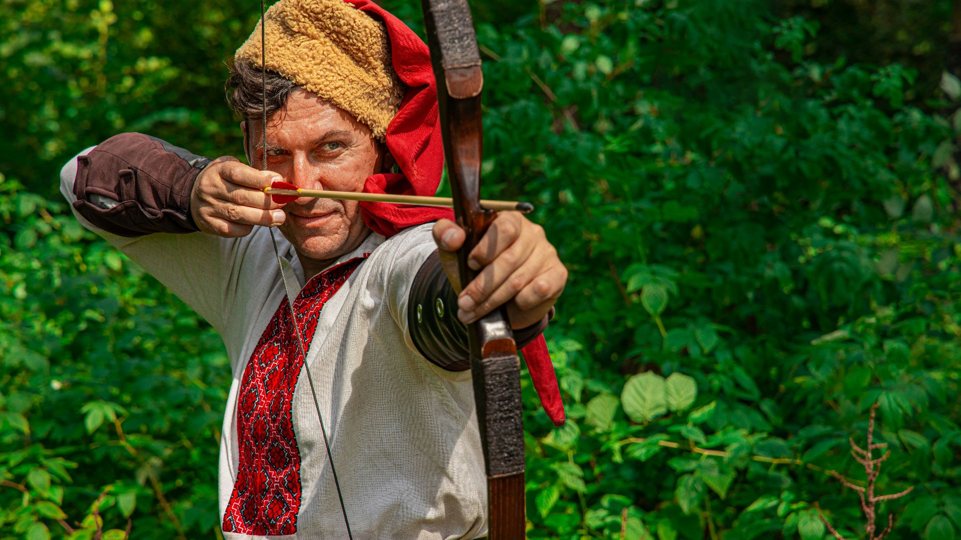 man in white shirt holding bow and arrow