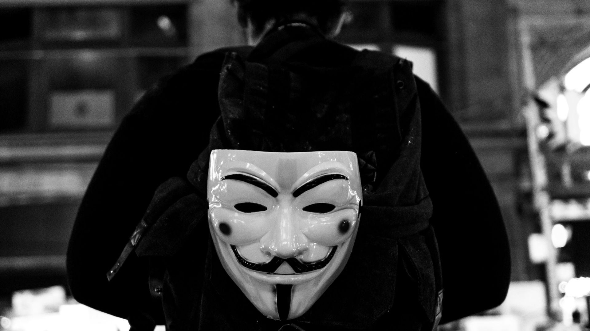 grayscale photography of person walking guy fawkes mask backpack