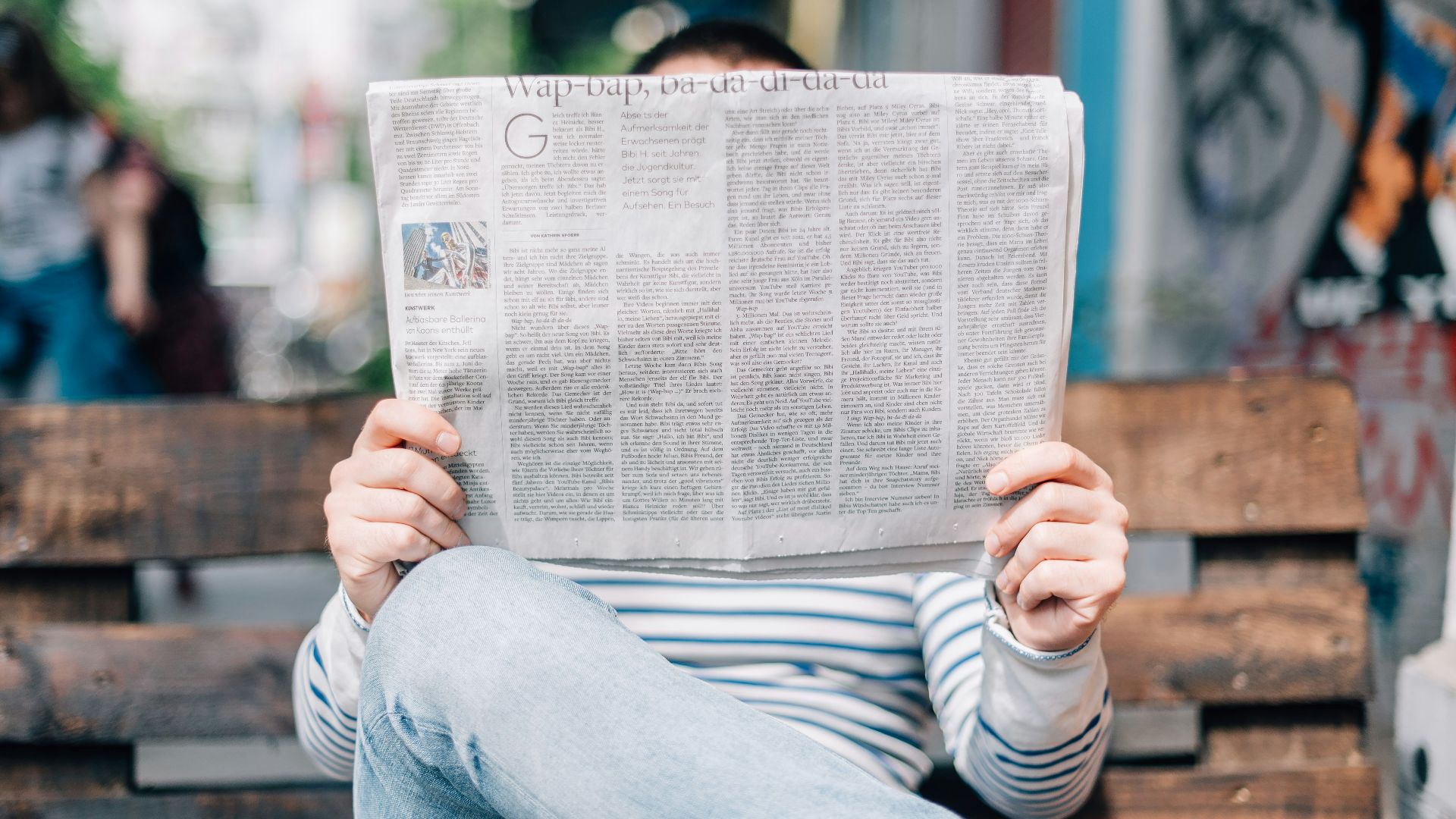 man sitting on bench reading newspaper