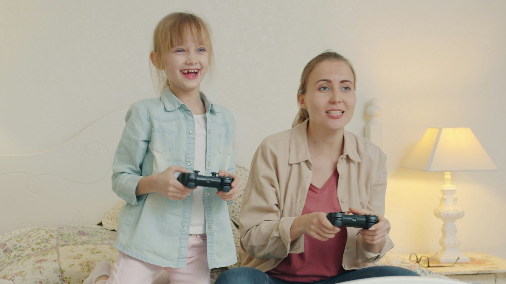 Mother and daughter playing video games together on bed