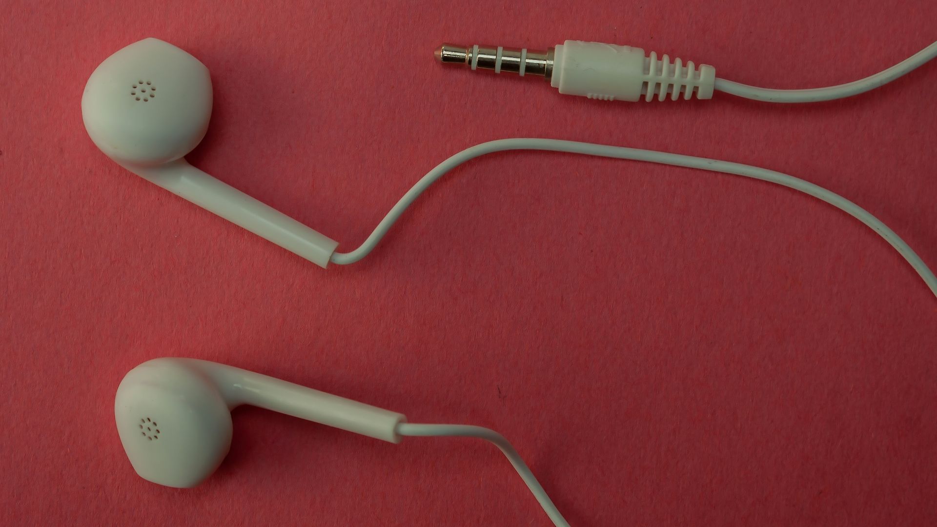 White earbuds and their cable on a pink surface.