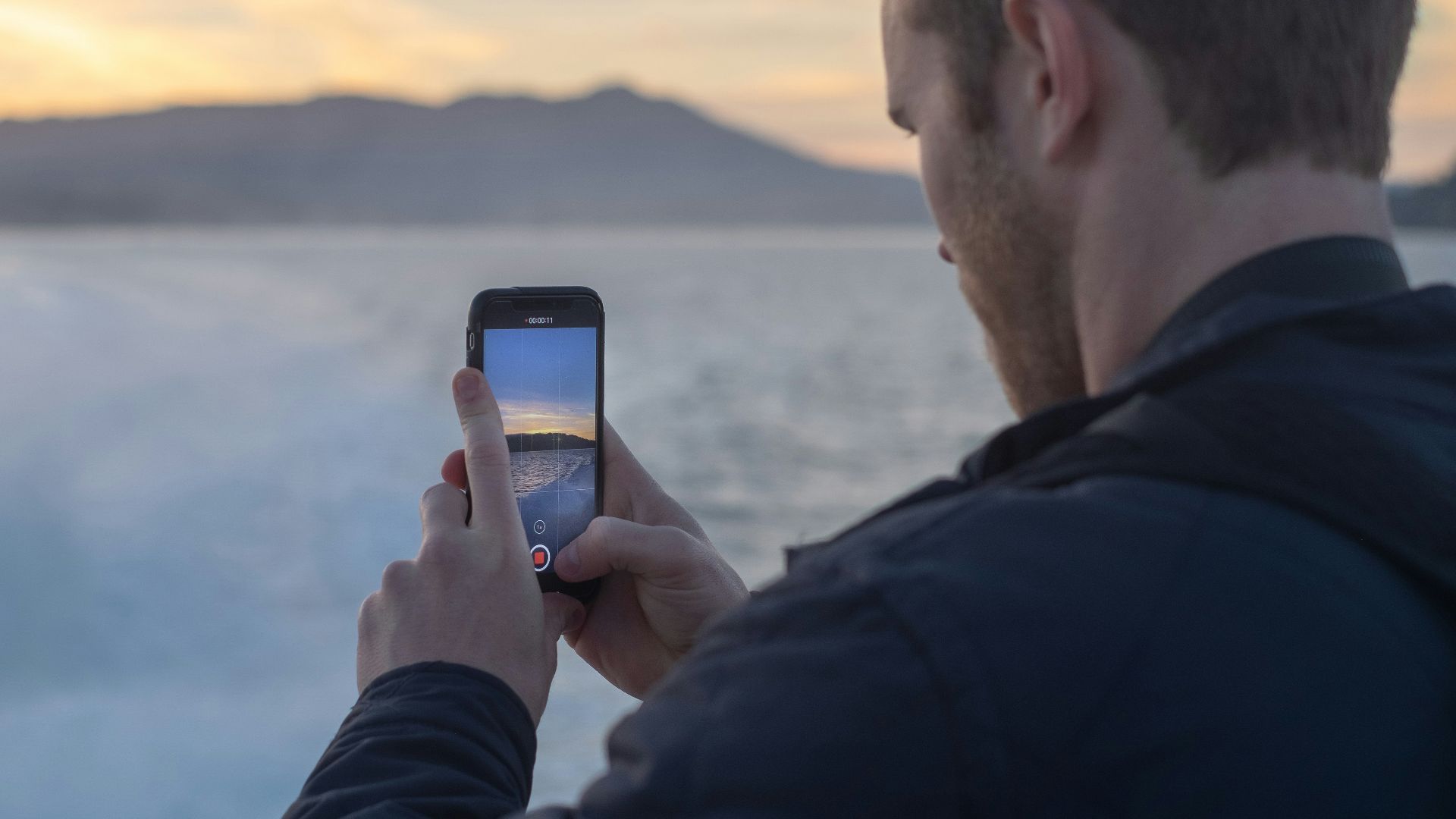 man taking photo of snow covered lake during sunrise