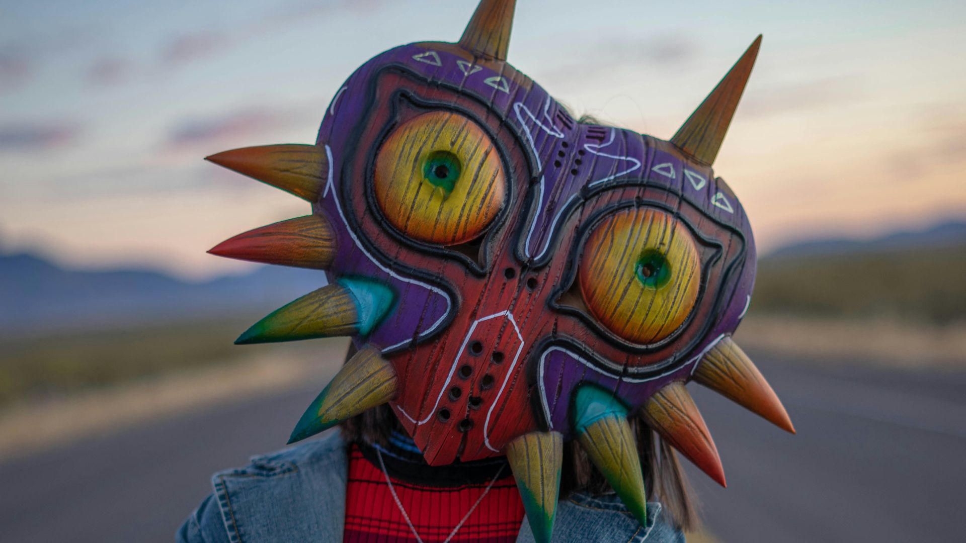person in blue denim jacket with yellow green and blue owl mask