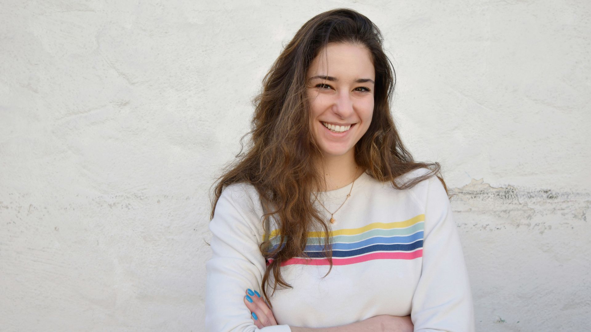 a woman standing with her arms crossed in front of a white wall