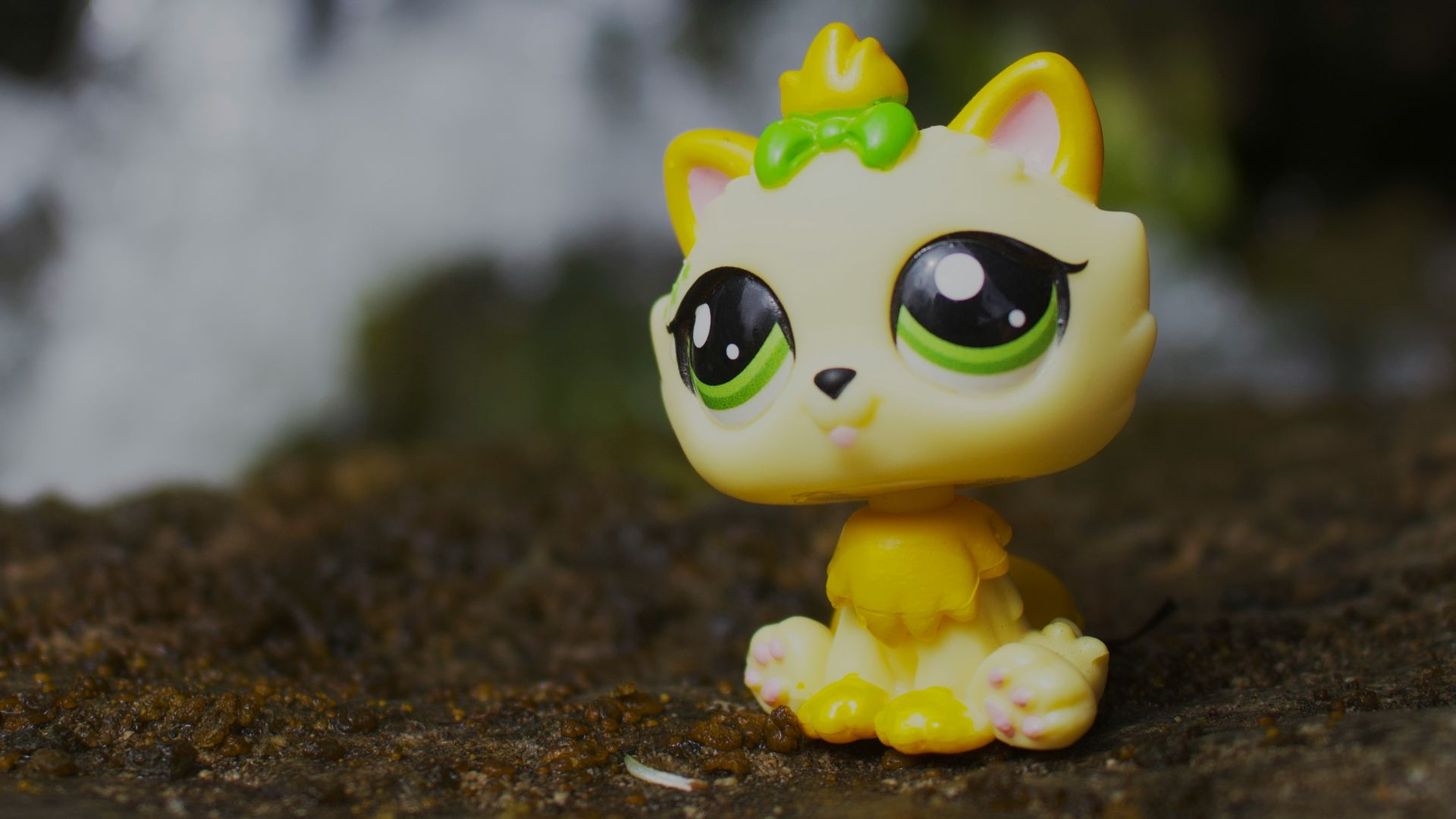 Yellow cat toy sits on dirt with waterfall background.