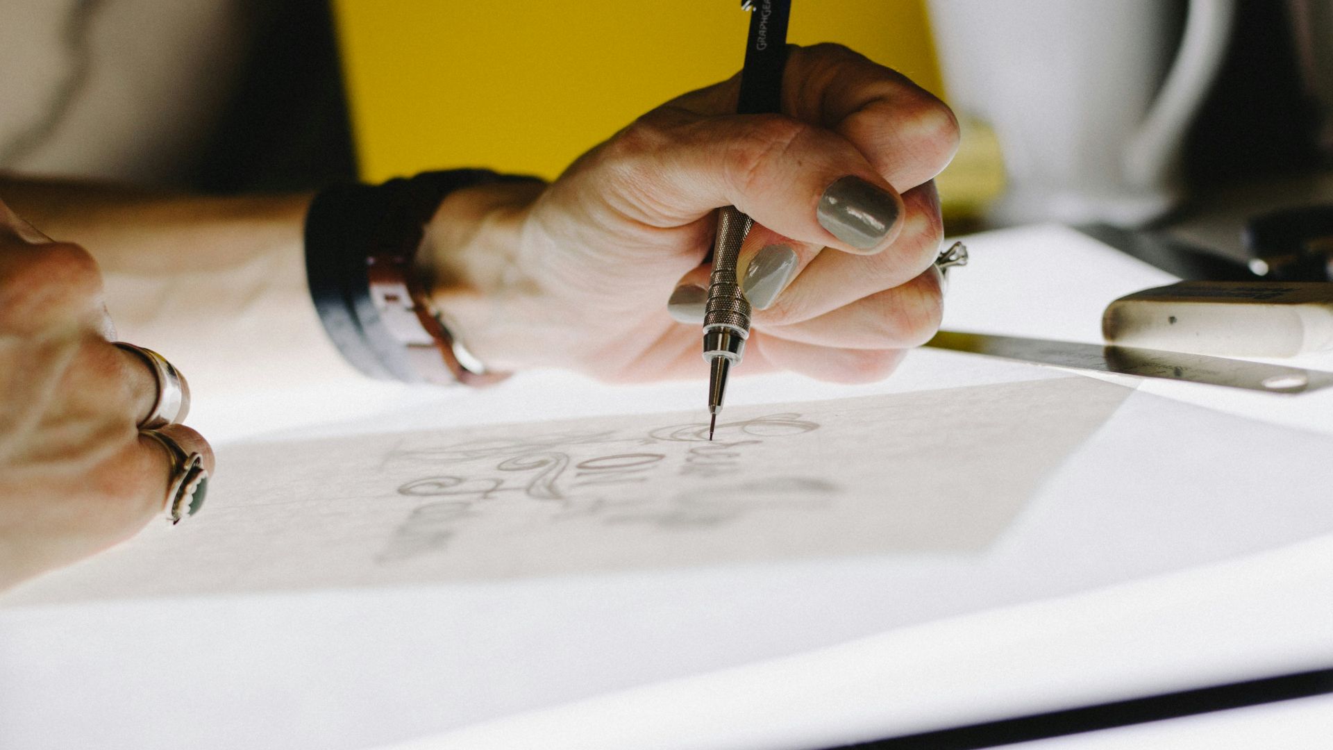 person lettering on tracing paper using mechanical pencil