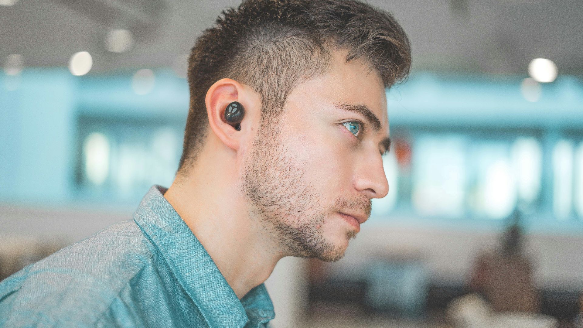 man wearing blue dress shirt with black Bluetooth earbuds
